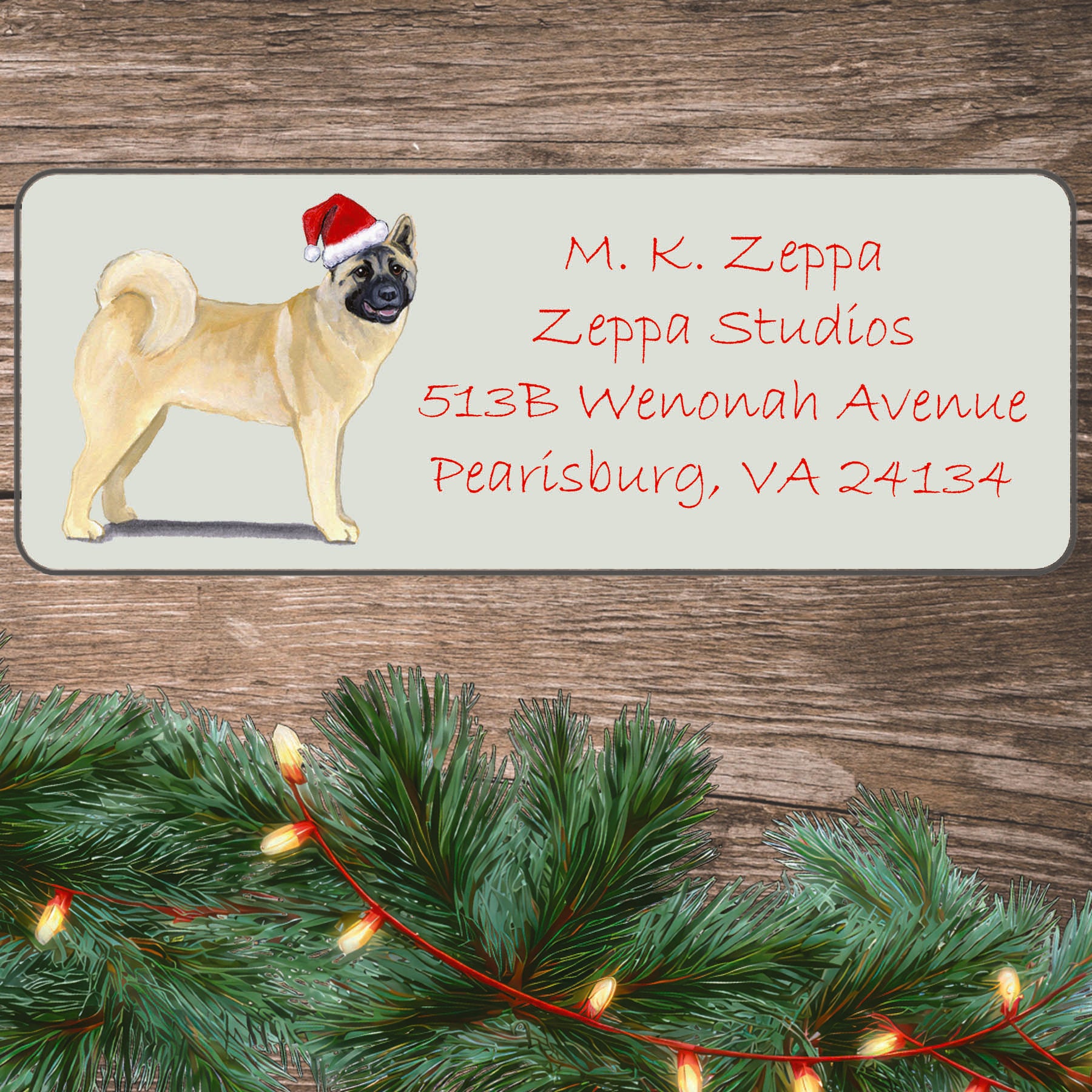 An illustration of an Akita wearing a Santa Hat on an ivory return address label set off by a wood surface with holiday greenery background.