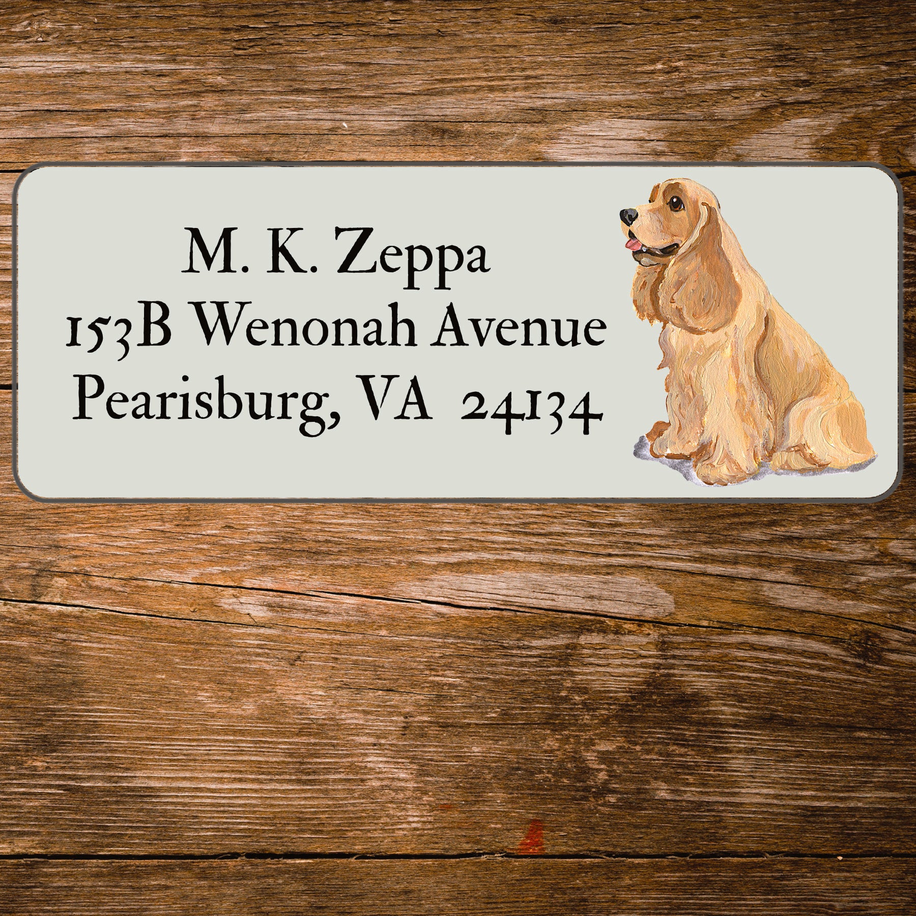 Address label with a Cocker Spaniel illustration and contact information on a wooden surface