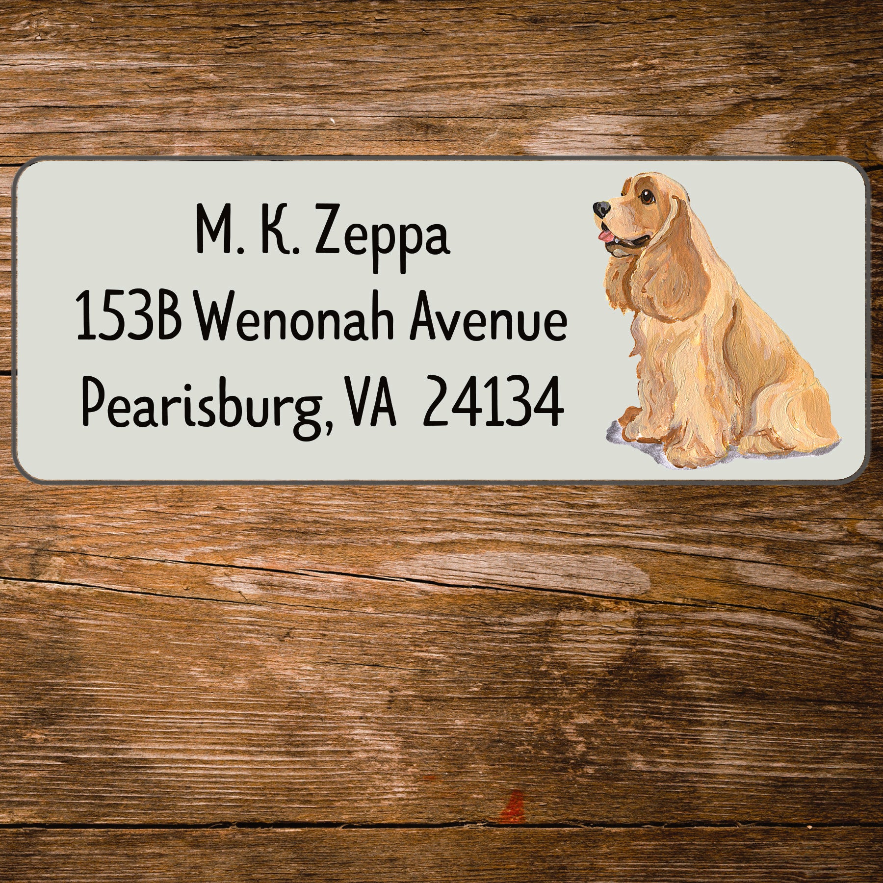 Address label with a Cocker Spaniel illustration and contact information on a wooden surface