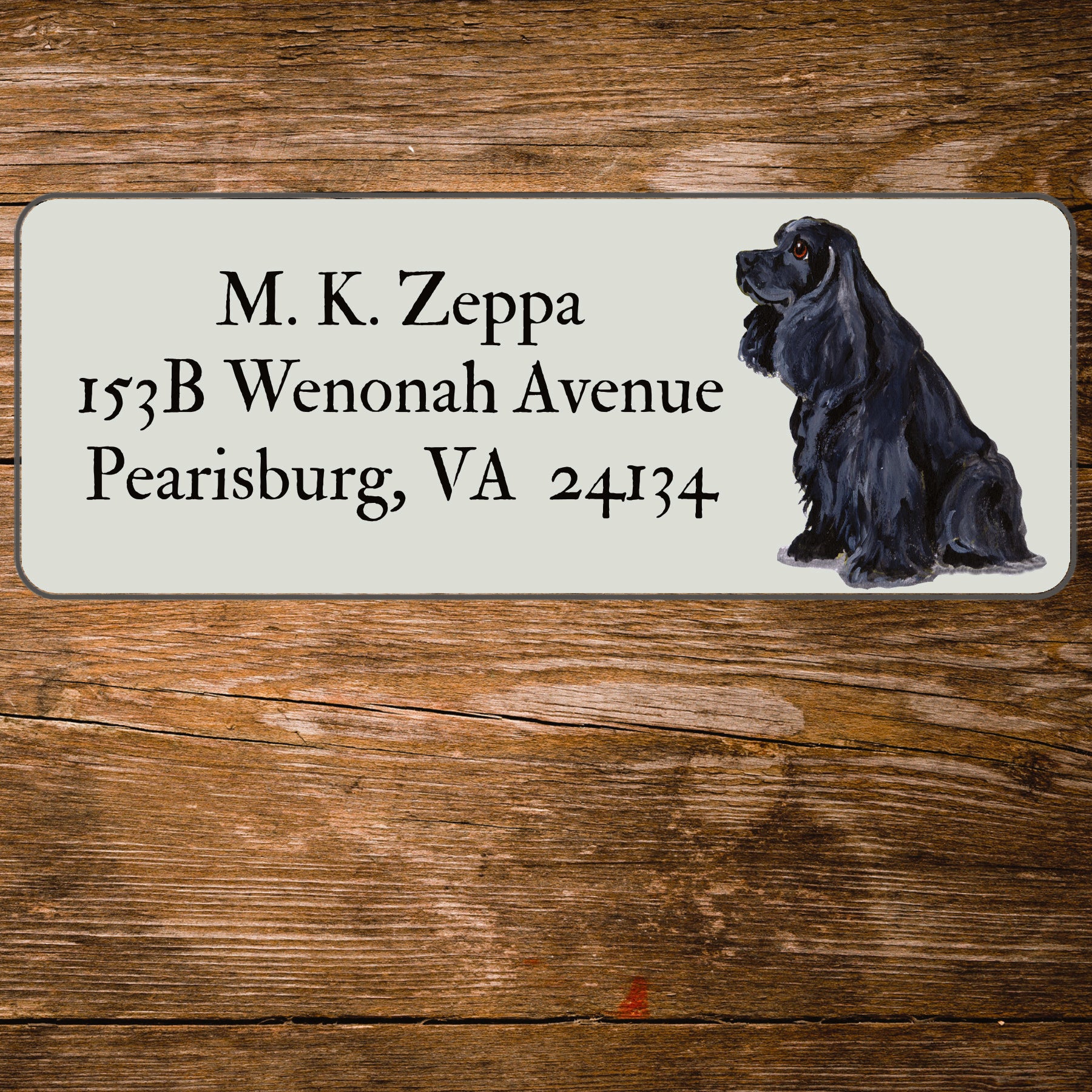 Address label with a Cocker Spaniel illustration and contact information on a wooden surface