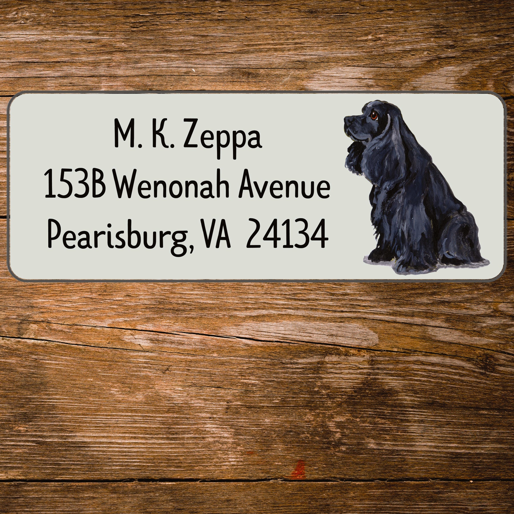 Address label with a Cocker Spaniel illustration and contact information on a wooden surface