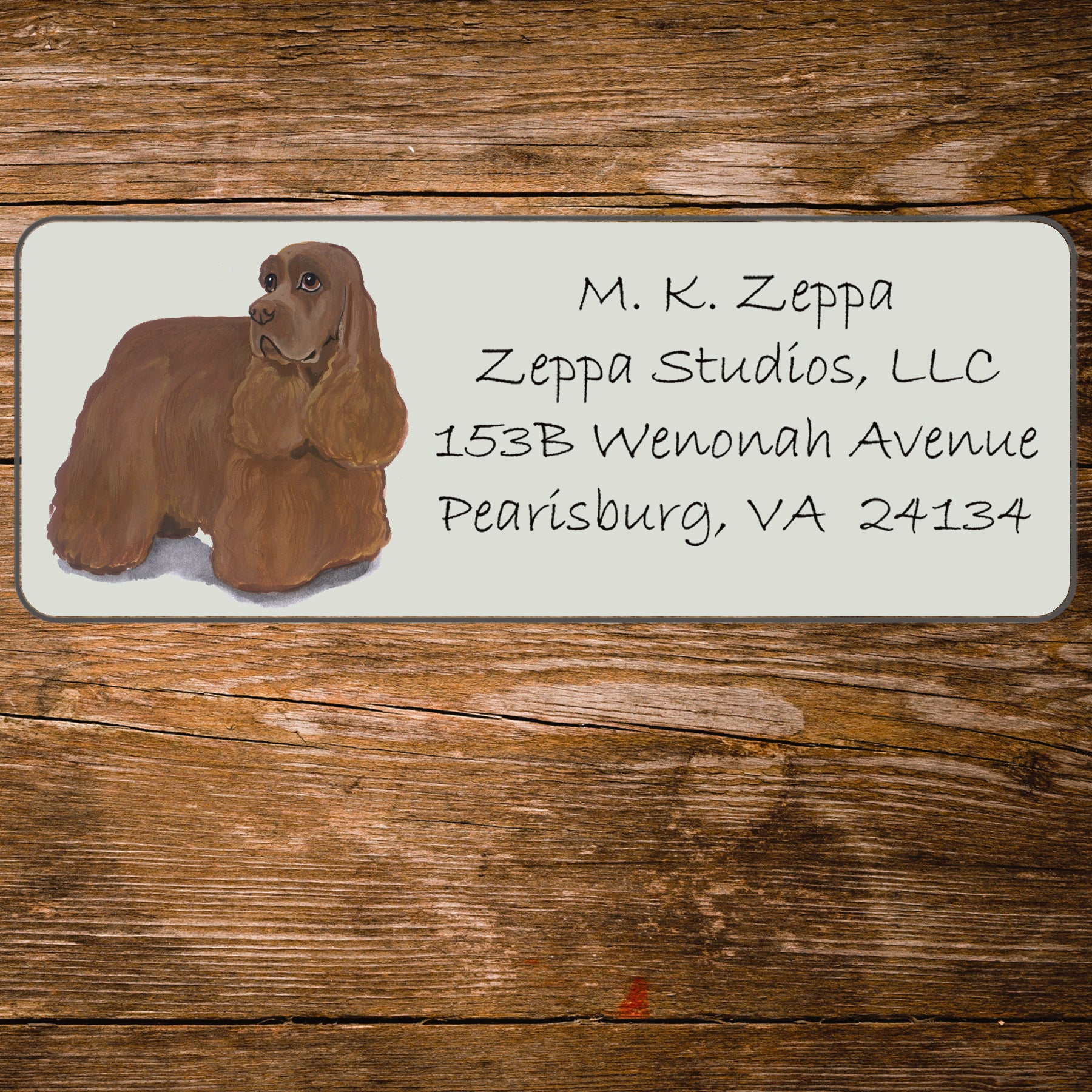 Address label with a Cocker Spaniel illustration and contact information on a wooden surface