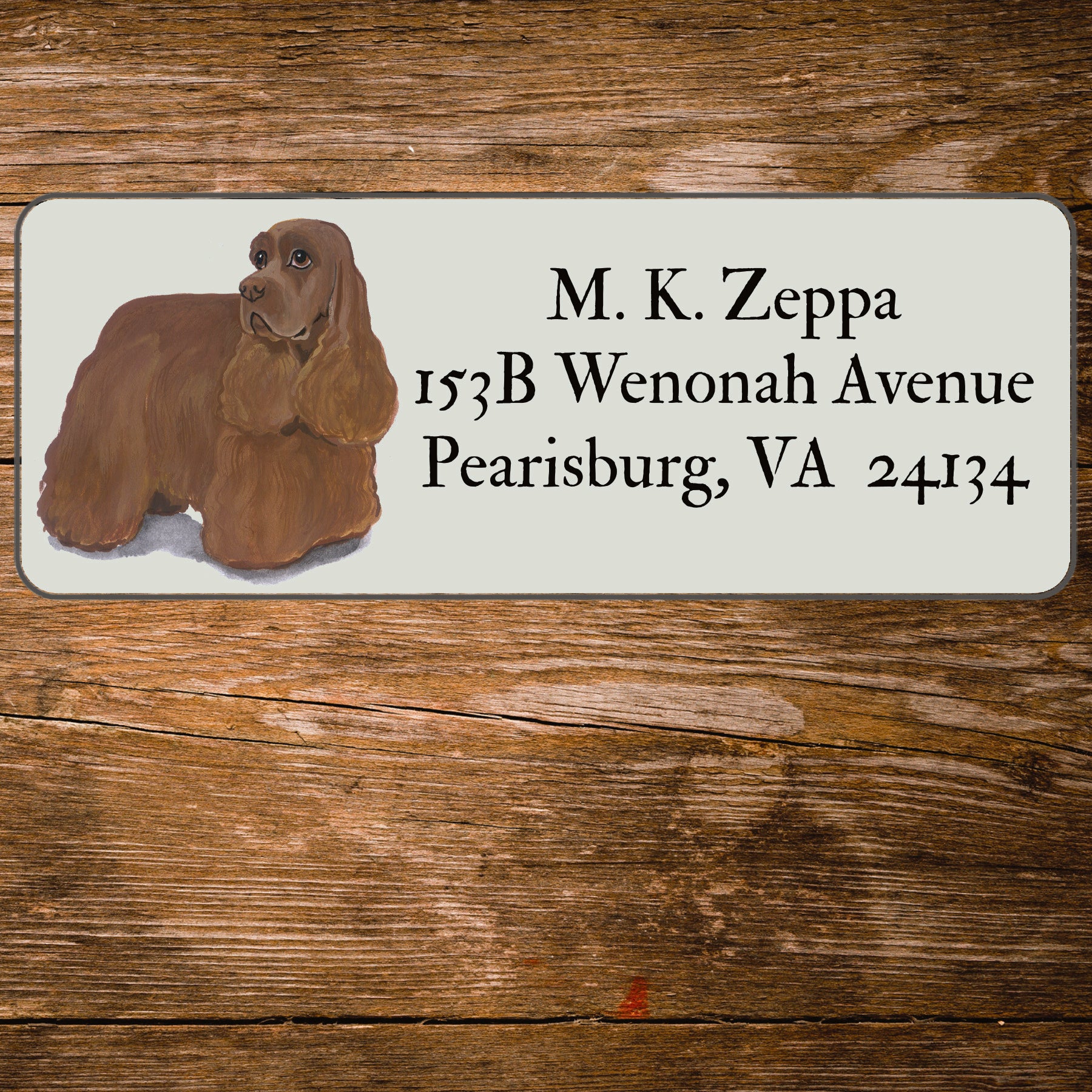 Address label with a Cocker Spaniel illustration and contact information on a wooden surface