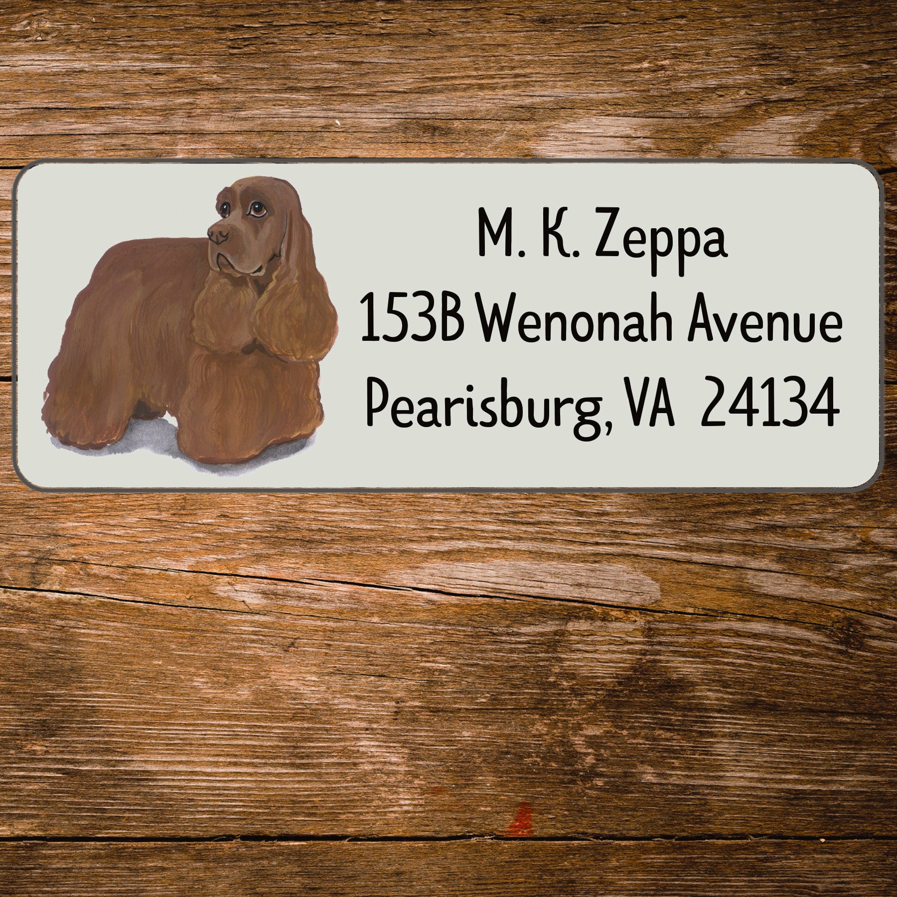 Address label with a Cocker Spaniel illustration and contact information on a wooden surface