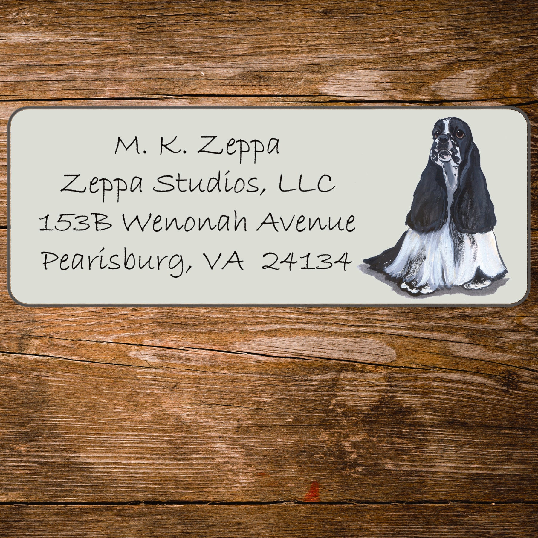 Address label with a Cocker Spaniel illustration and contact information on a wooden surface