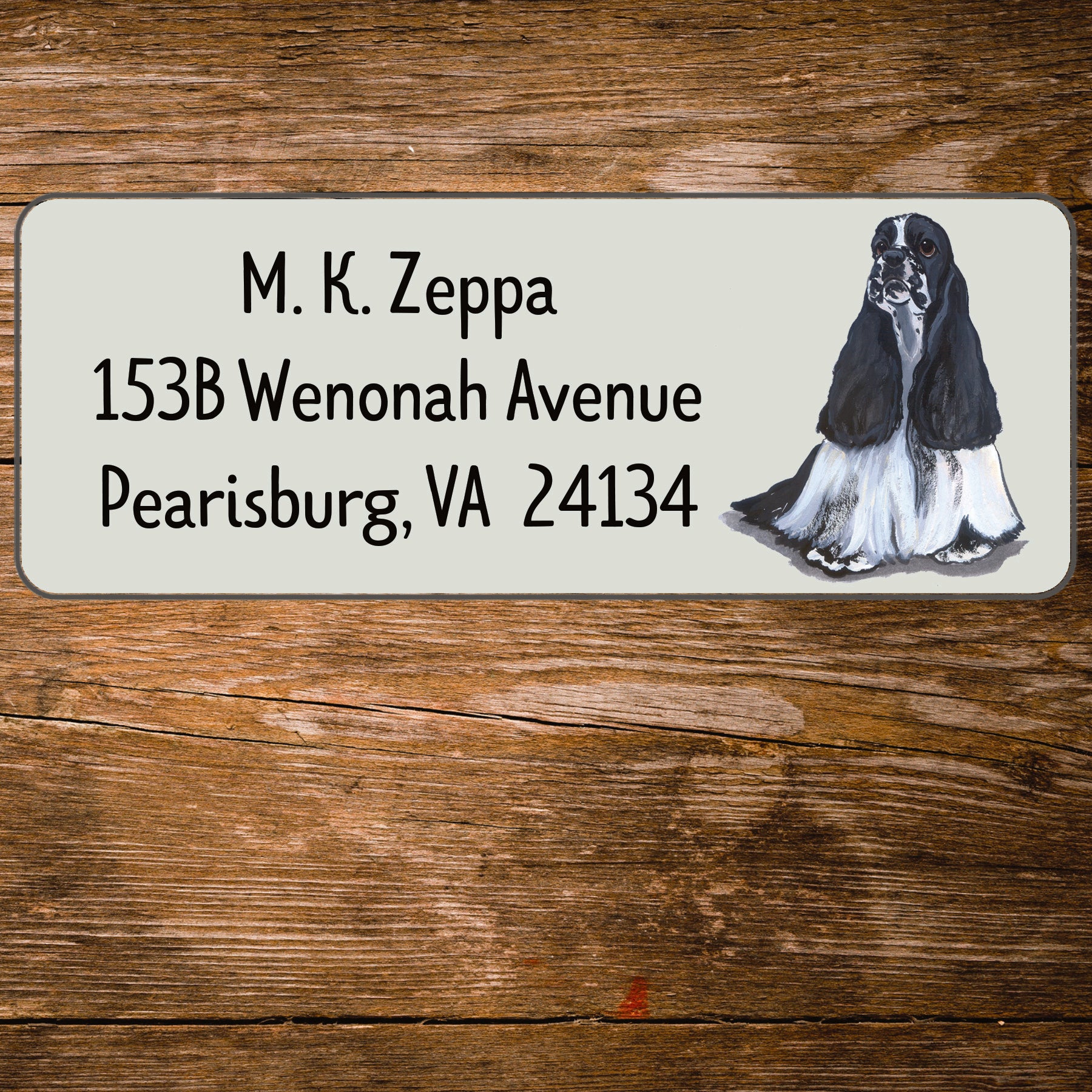 Address label with a Cocker Spaniel illustration and contact information on a wooden surface