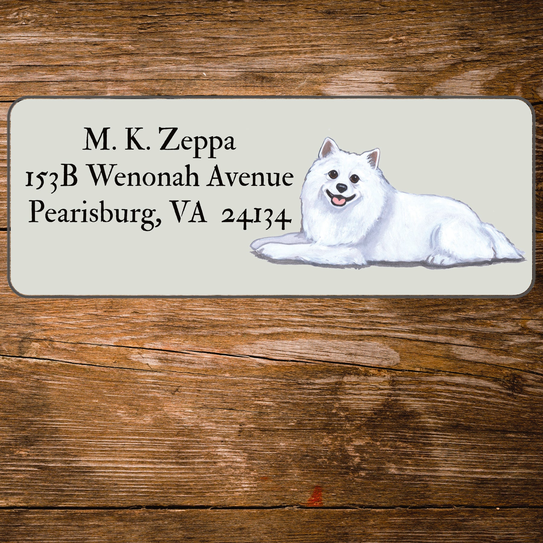Return address label with an American Eskimo Dog illustration on a wooden surface