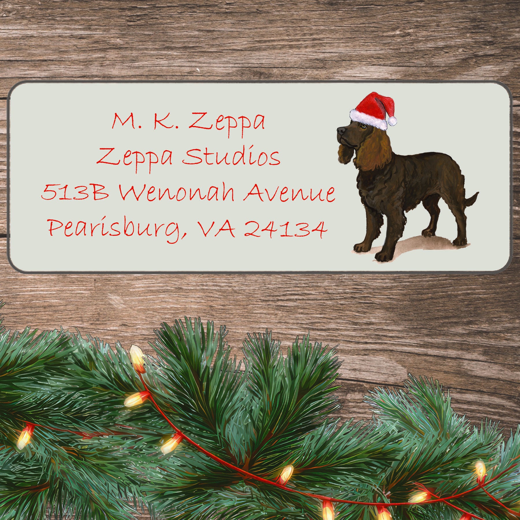 An illustration of an American Water Spaniel wearing a Santa Hat on an ivory return address label set off by a wood surface with holiday greenery background.