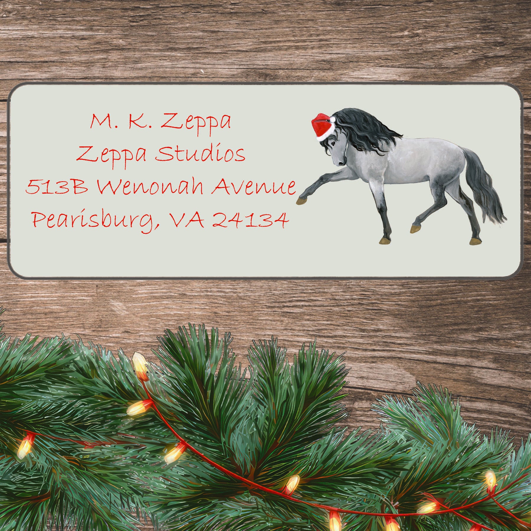 An illustration of a Andalusian Horse wearing a Santa Hat on an ivory return address label set off by a wood surface with holiday greenery background.