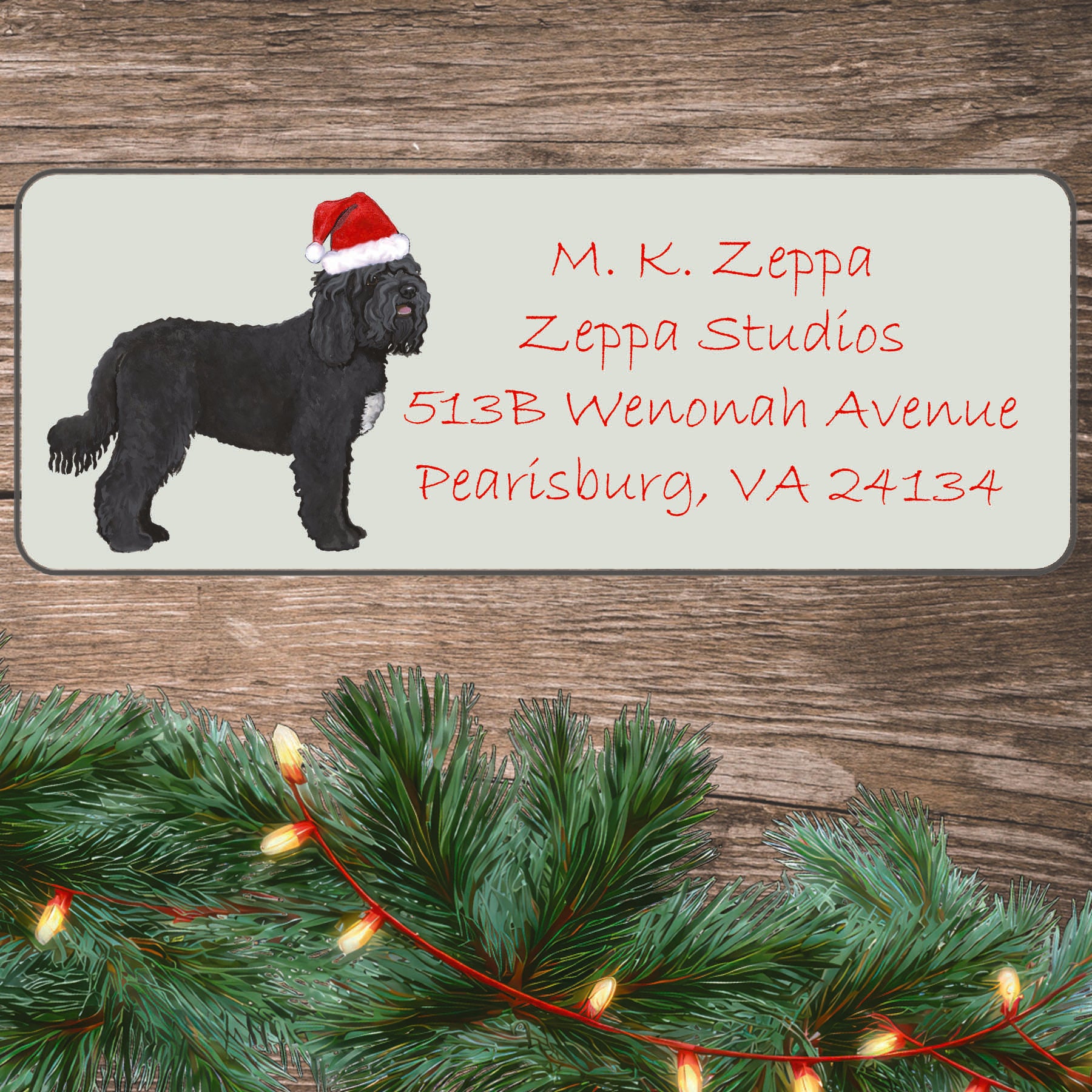 A Barbet in a Santa Hat illustration on an ivory return address label set off by a wood surface with holiday greenery background.