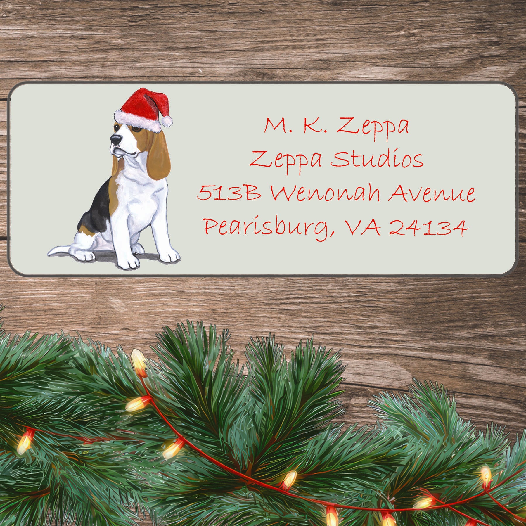 An illustration of a Beagle puppy wearing a Santa Hat on an ivory return address label set off by a wood surface with holiday greenery background.