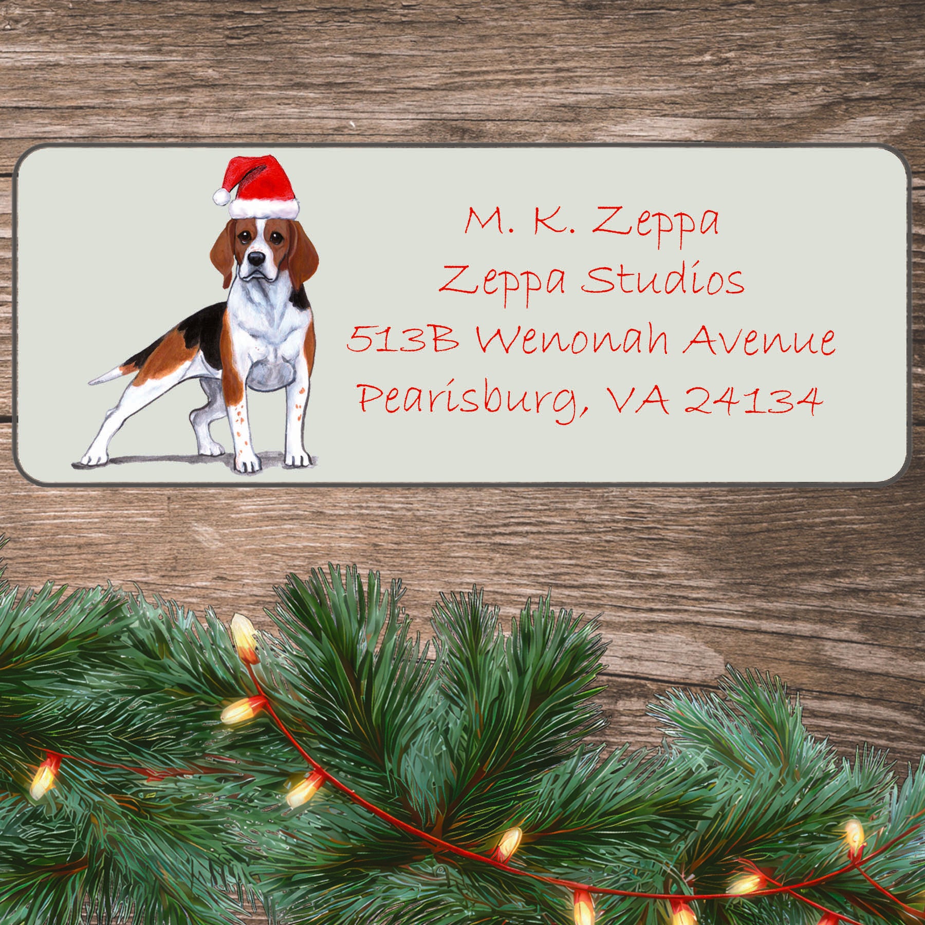 An illustration of a Beagle wearing a Santa Hat on an ivory return address label set off by a wood surface with holiday greenery background.