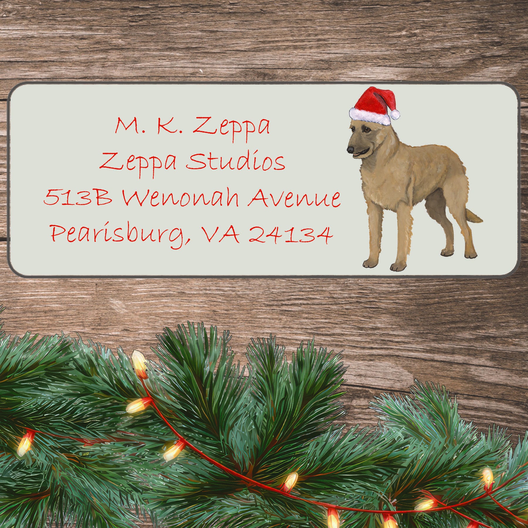 An illustration of a Belgian Laekenois wearing a Santa Hat on an ivory return address label set off by a wood surface with holiday greenery background.