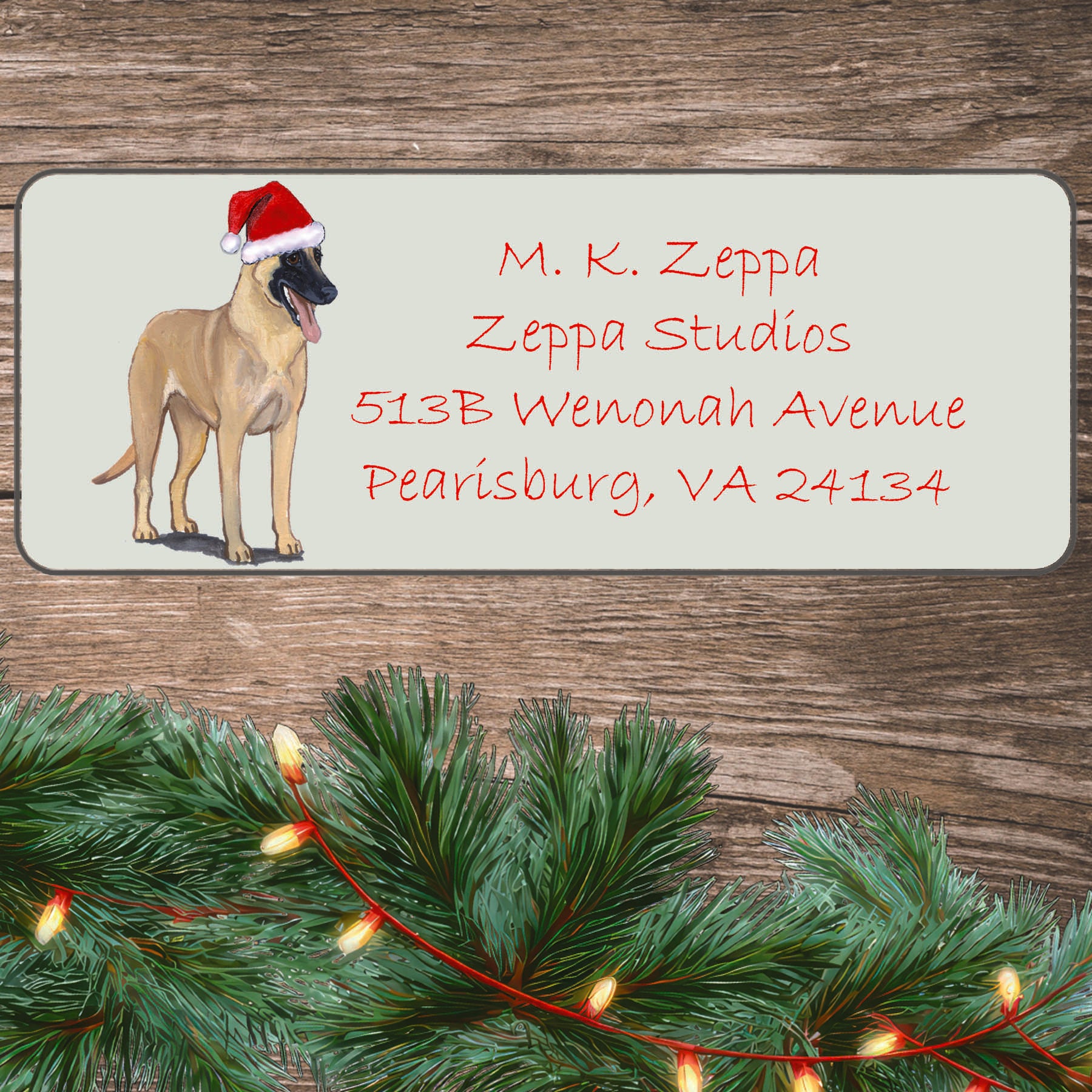 An illustration of a Belgian Malinois wearing a Santa Hat on an ivory return address label set off by a wood surface with holiday greenery background.