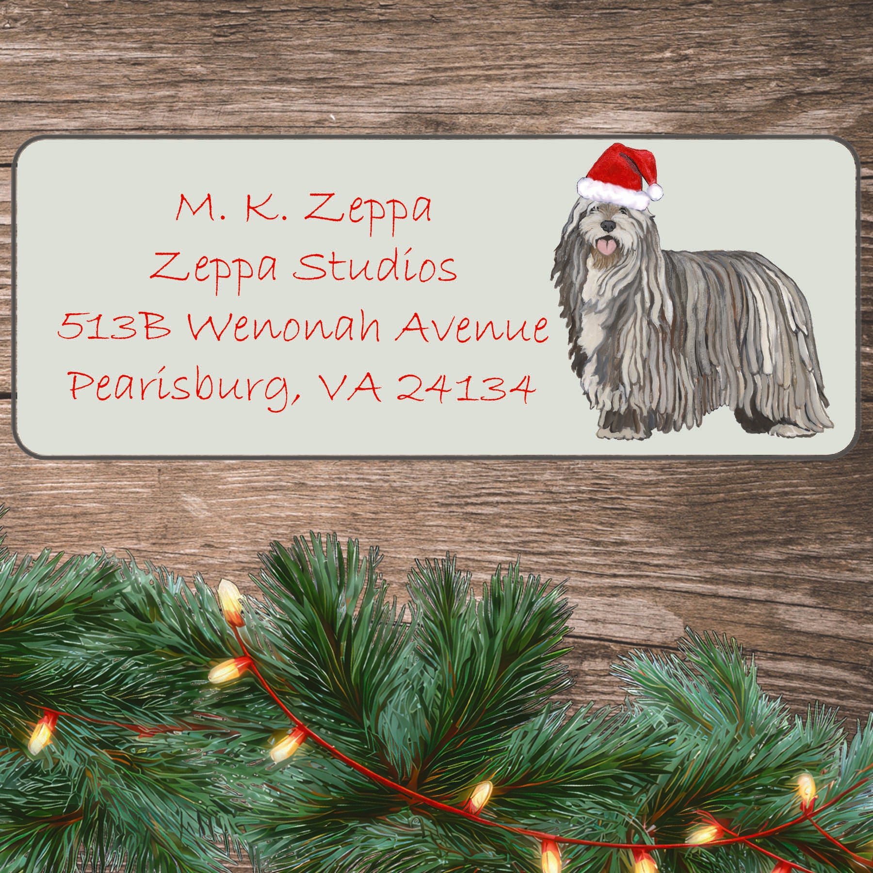 A Bergamasco in a Santa Hat illustration on an ivory return address label set off by a wood surface with holiday greenery background.