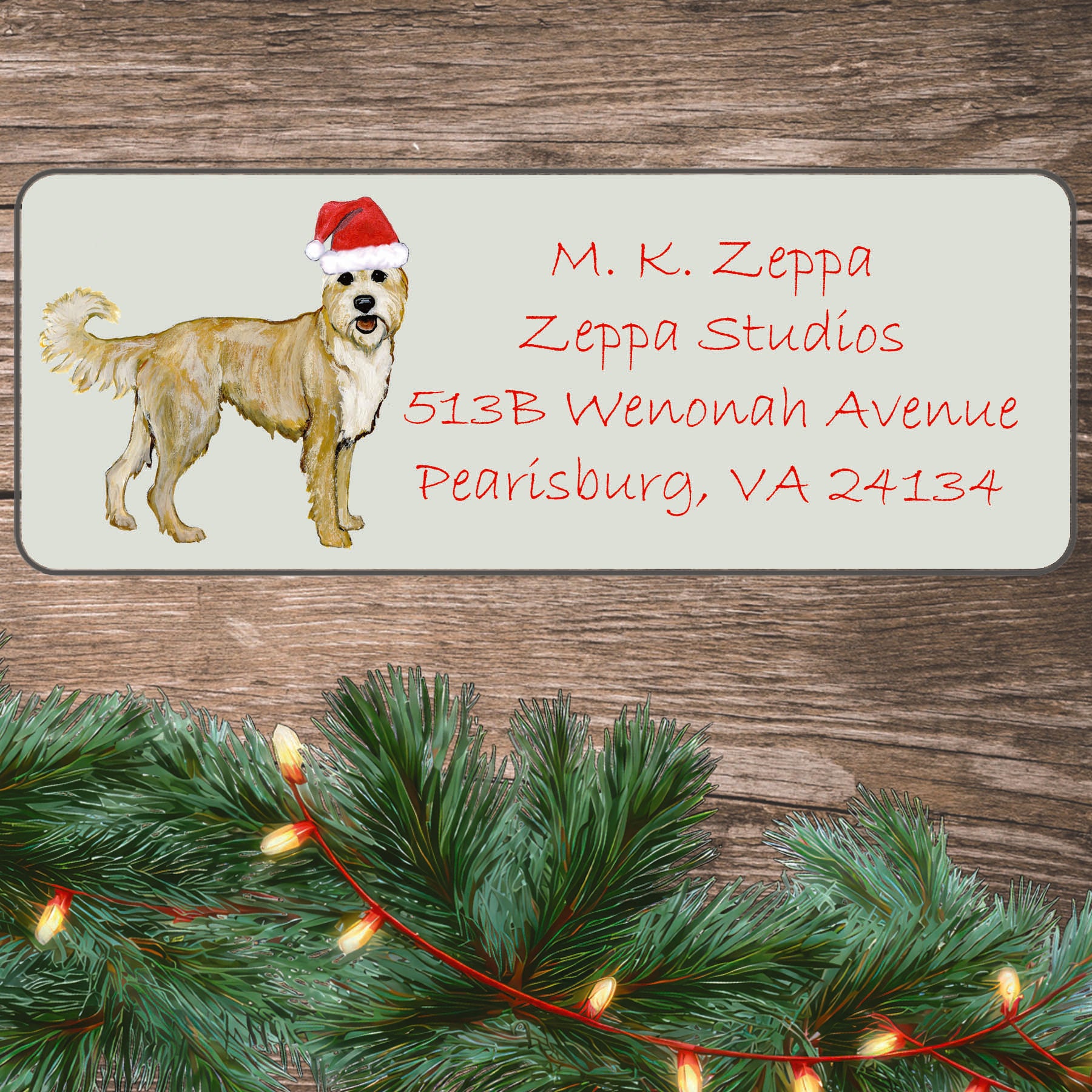 A Berger Picard in a Santa Hat illustration on an ivory return address label set off by a wood surface with holiday greenery background.