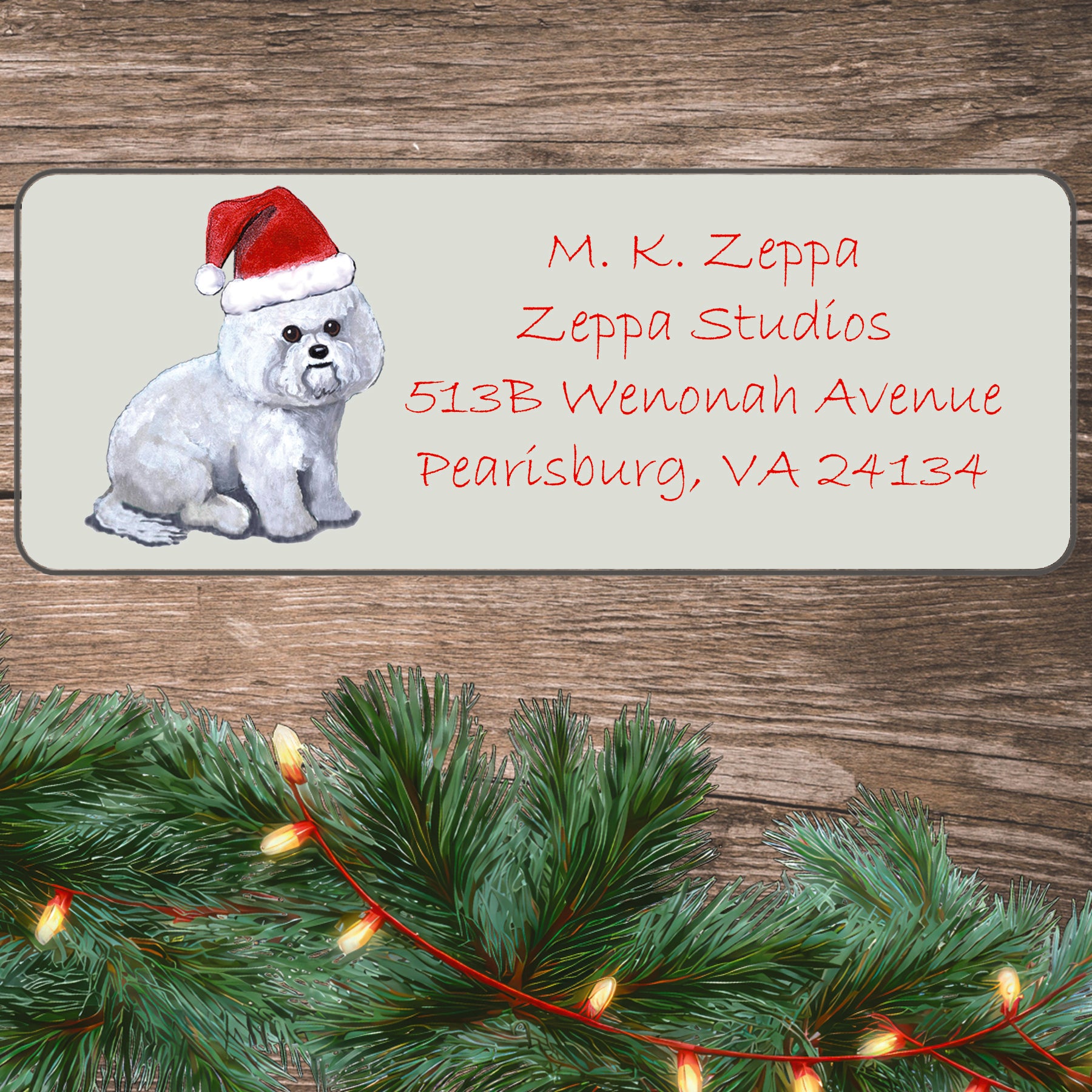 An illustration of a Bichon Frise wearing a Santa Hat on an ivory return address label set off by a wood surface with holiday greenery background.