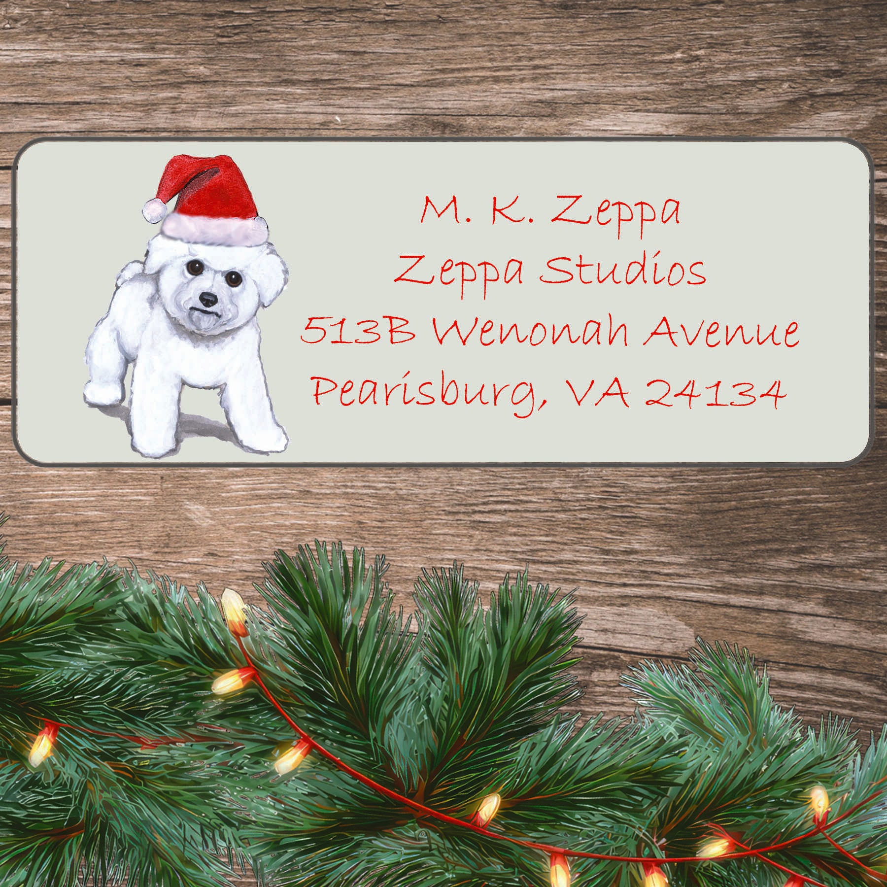An illustration of a Bichon Frise puppy wearing a Santa Hat on an ivory return address label set off by a wood surface with holiday greenery background.