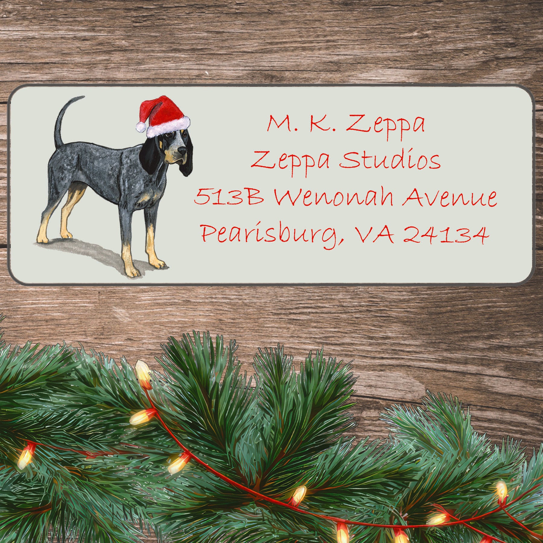 An illustration of a Bluetick Coonhound wearing a Santa Hat on an ivory return address label set off by a wood surface with holiday greenery background.