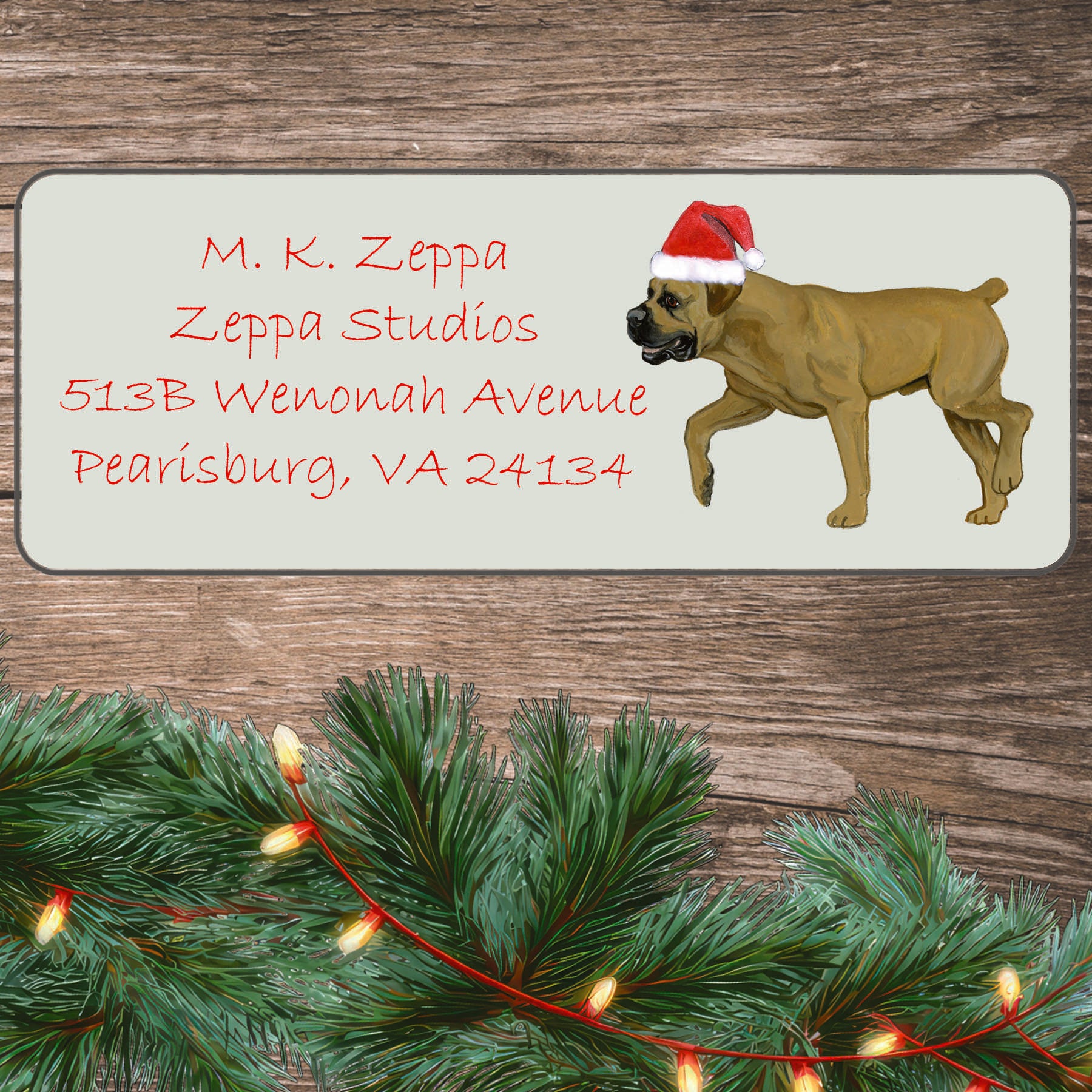 An illustration of a Boerboel wearing a Santa Hat on an ivory return address label set off by a wood surface with holiday greenery background.