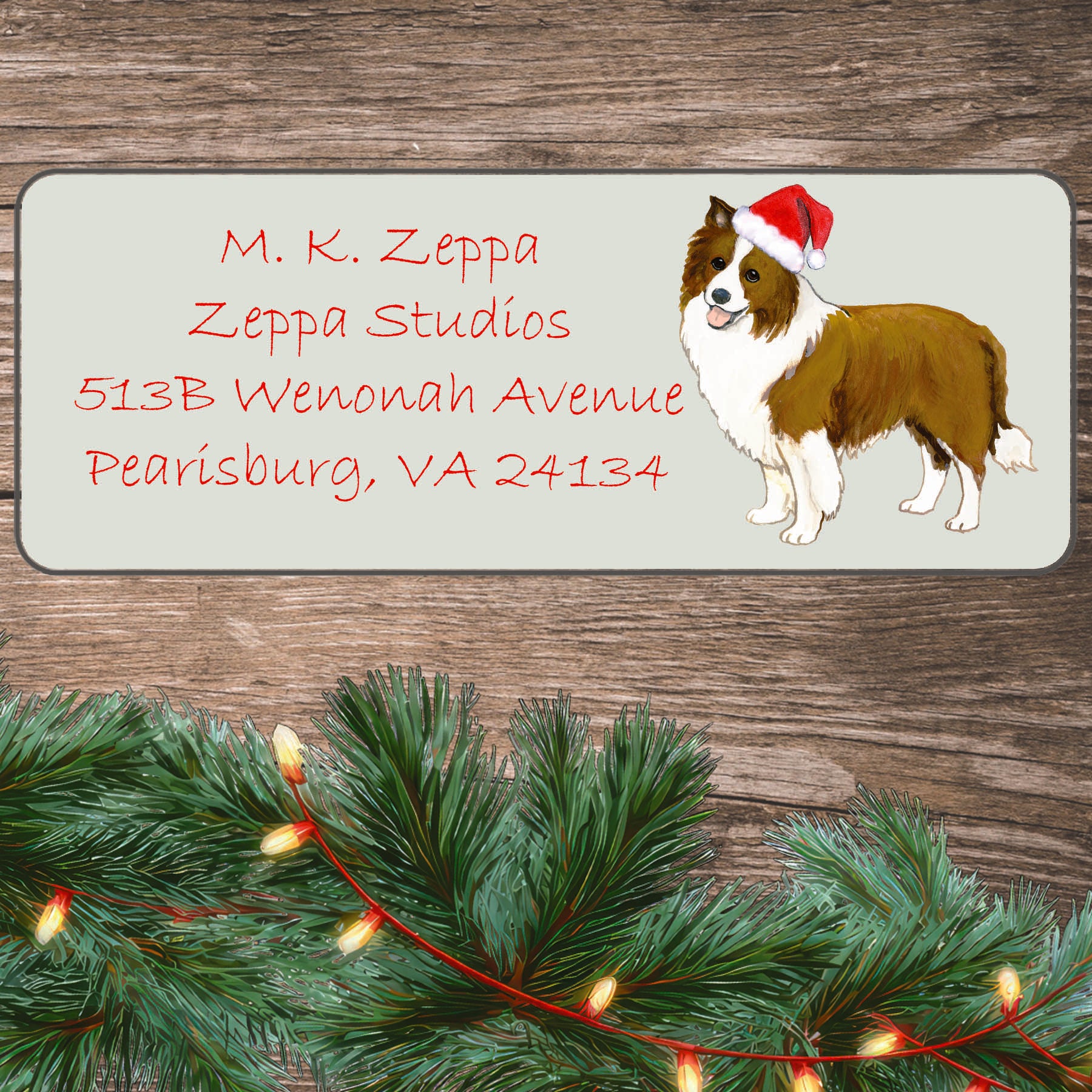 An illustration of a brown and white Border Collie wearing a Santa Hat on an ivory return address label set off by a wood surface with holiday greenery background.