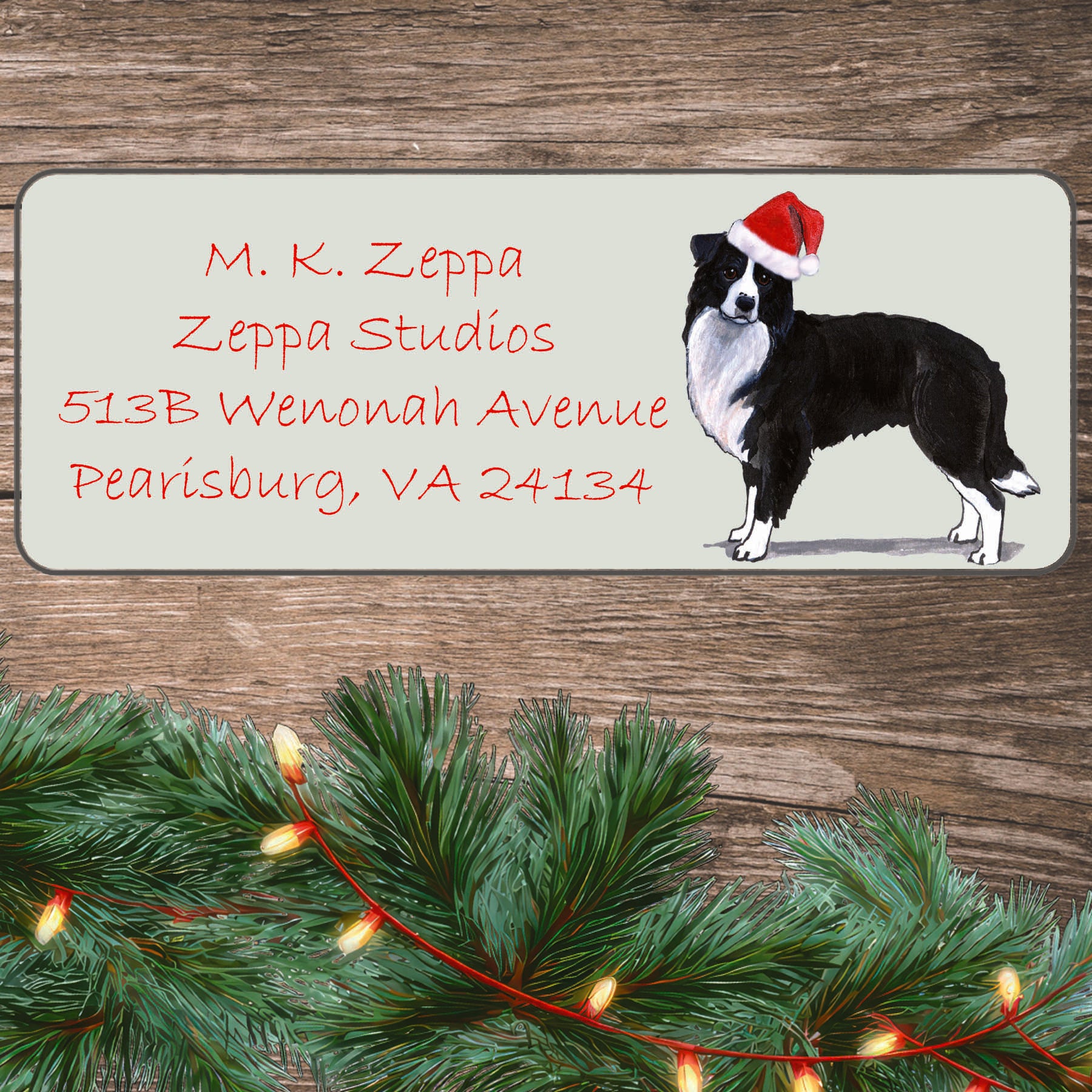 An illustration of a Border Collie wearing a Santa Hat on an ivory return address label set off by a wood surface with holiday greenery background.