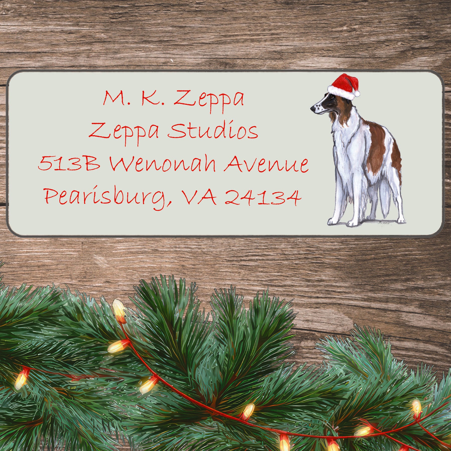 An illustration of a Borzoi wearing a Santa Hat on an ivory return address label set off by a wood surface with holiday greenery background.