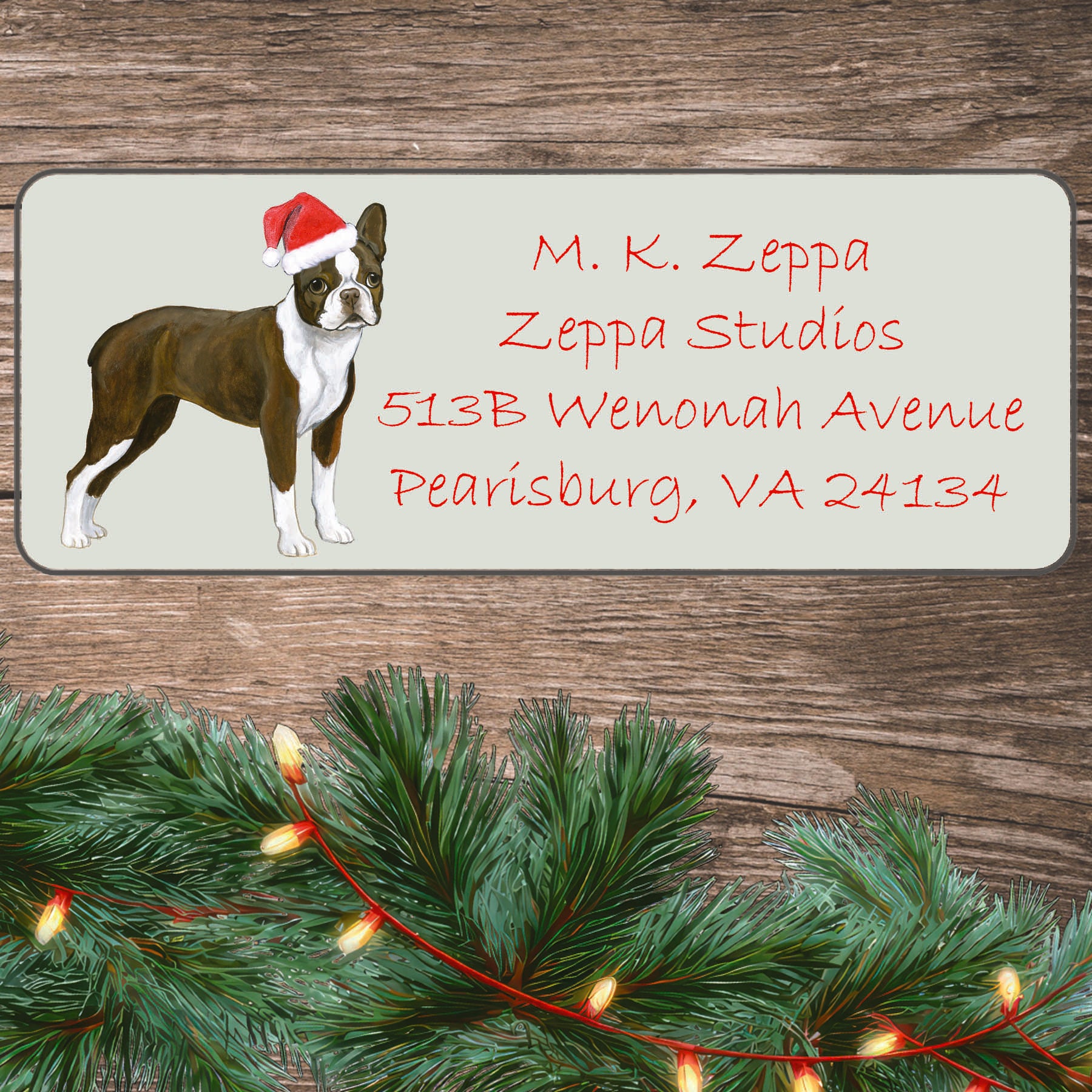 An illustration of a liver and white Boston Terrier wearing a Santa Hat on an ivory return address label set off by a wood surface with holiday greenery background.