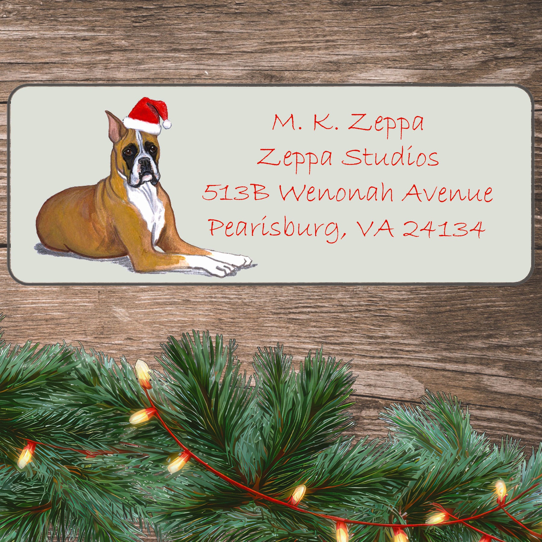 An illustration of a tan Boxer wearing a Santa Hat on an ivory return address label set off by a wood surface with holiday greenery background.
