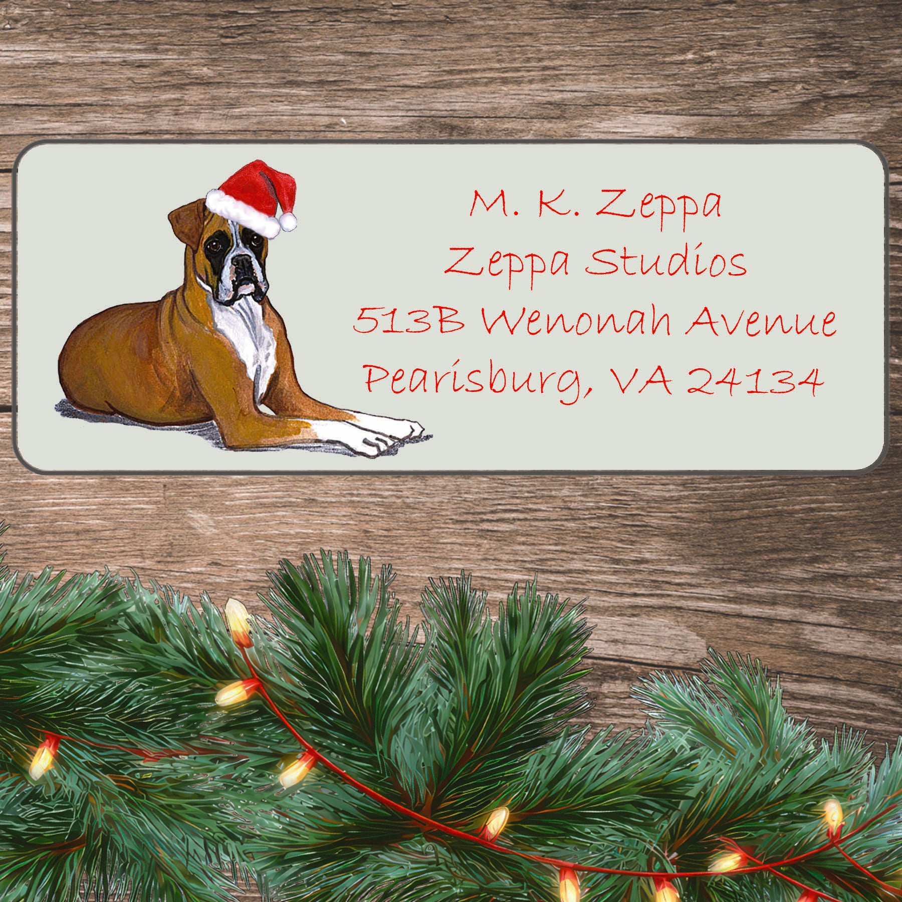 An illustration of an uncropped tan Boxer wearing a Santa Hat on an ivory return address label set off by a wood surface with holiday greenery background.