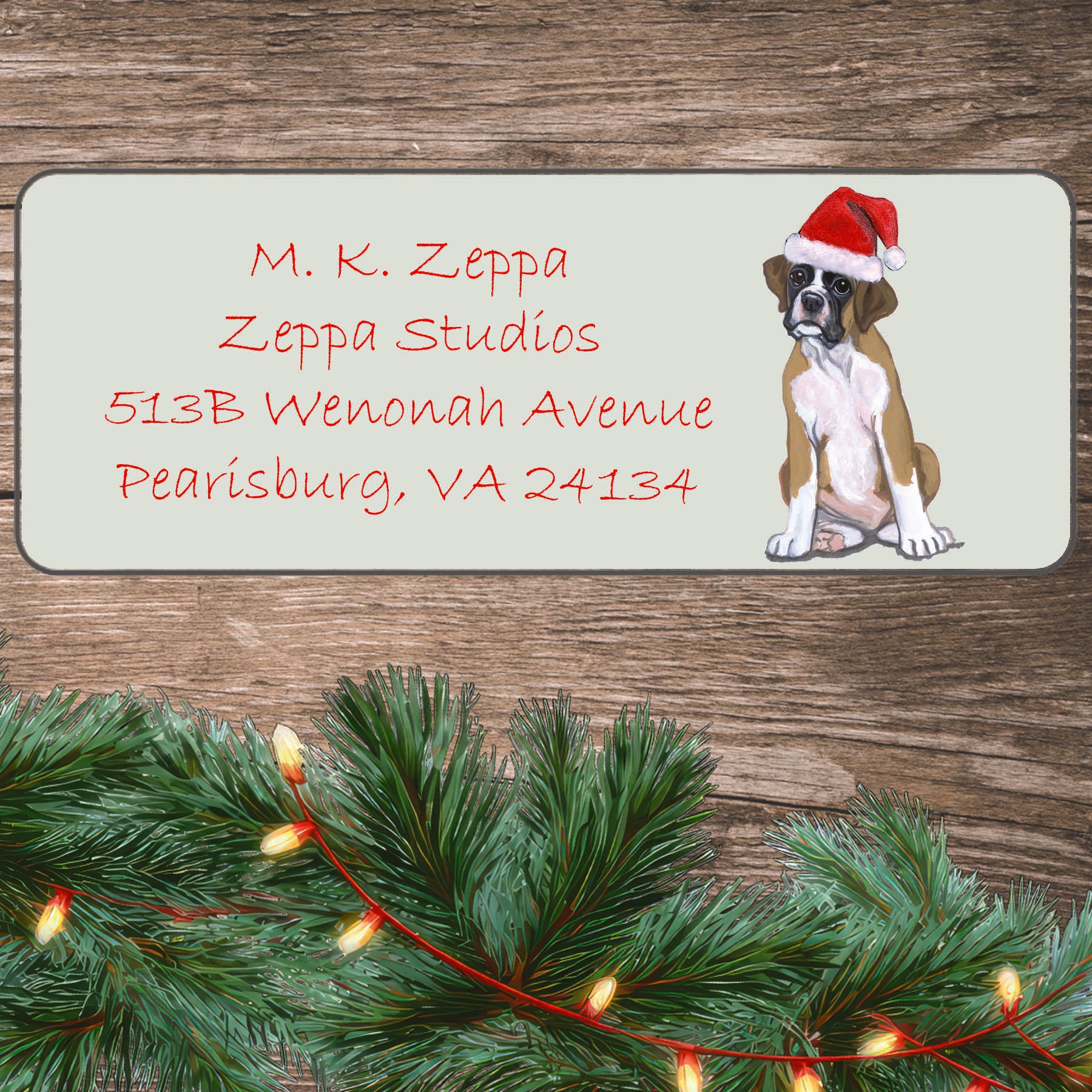 An illustration of a Boxer puppy  wearing a Santa Hat on an ivory return address label set off by a wood surface with holiday greenery background.