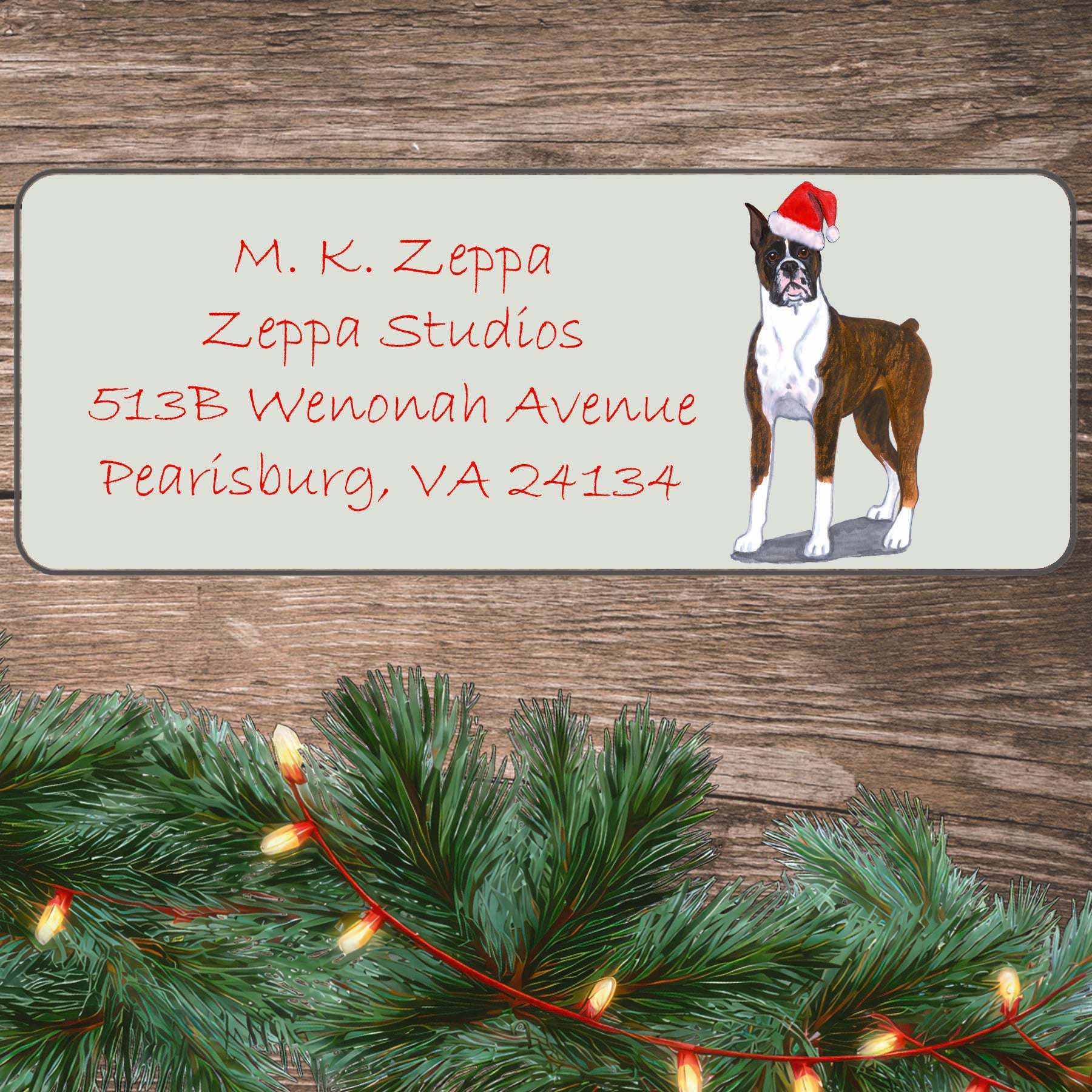 An illustration of a brindle Boxer wearing a Santa Hat on an ivory return address label set off by a wood surface with holiday greenery background.