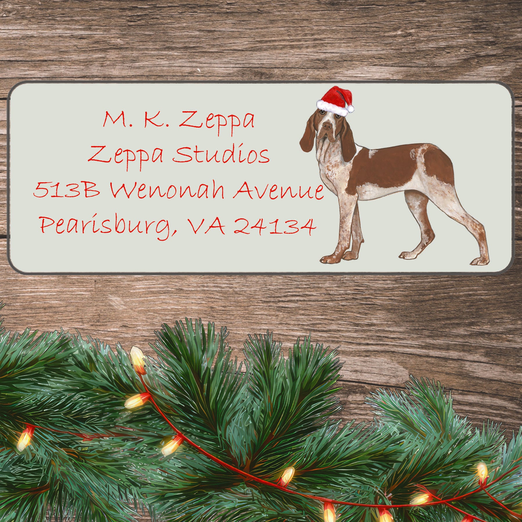 A Bracco Italiano in a Santa Hat illustration on an ivory return address label set off by a wood surface with holiday greenery background.