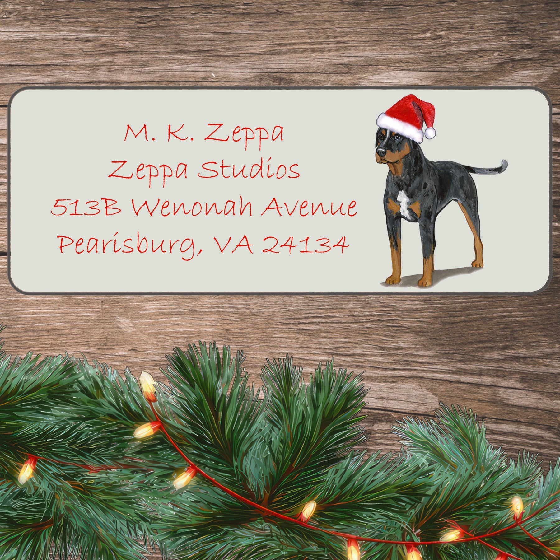 An illustration of a Catahoula Leopard Dog wearing a Santa Hat on an ivory return address label set off by a wood surface with holiday greenery background.