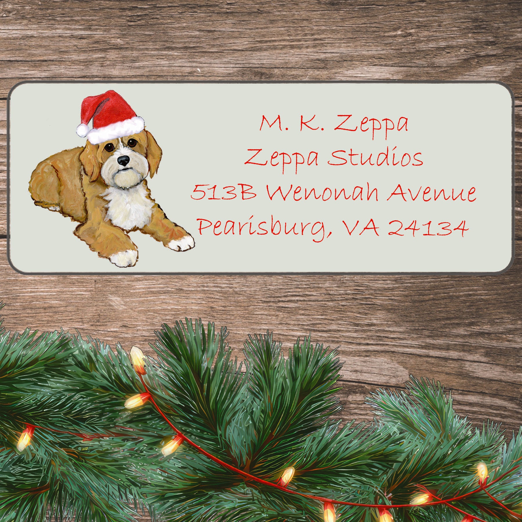 An illustration of a Cavapoo wearing a Santa Hat on an ivory return address label set off by a wood surface with holiday greenery background.
