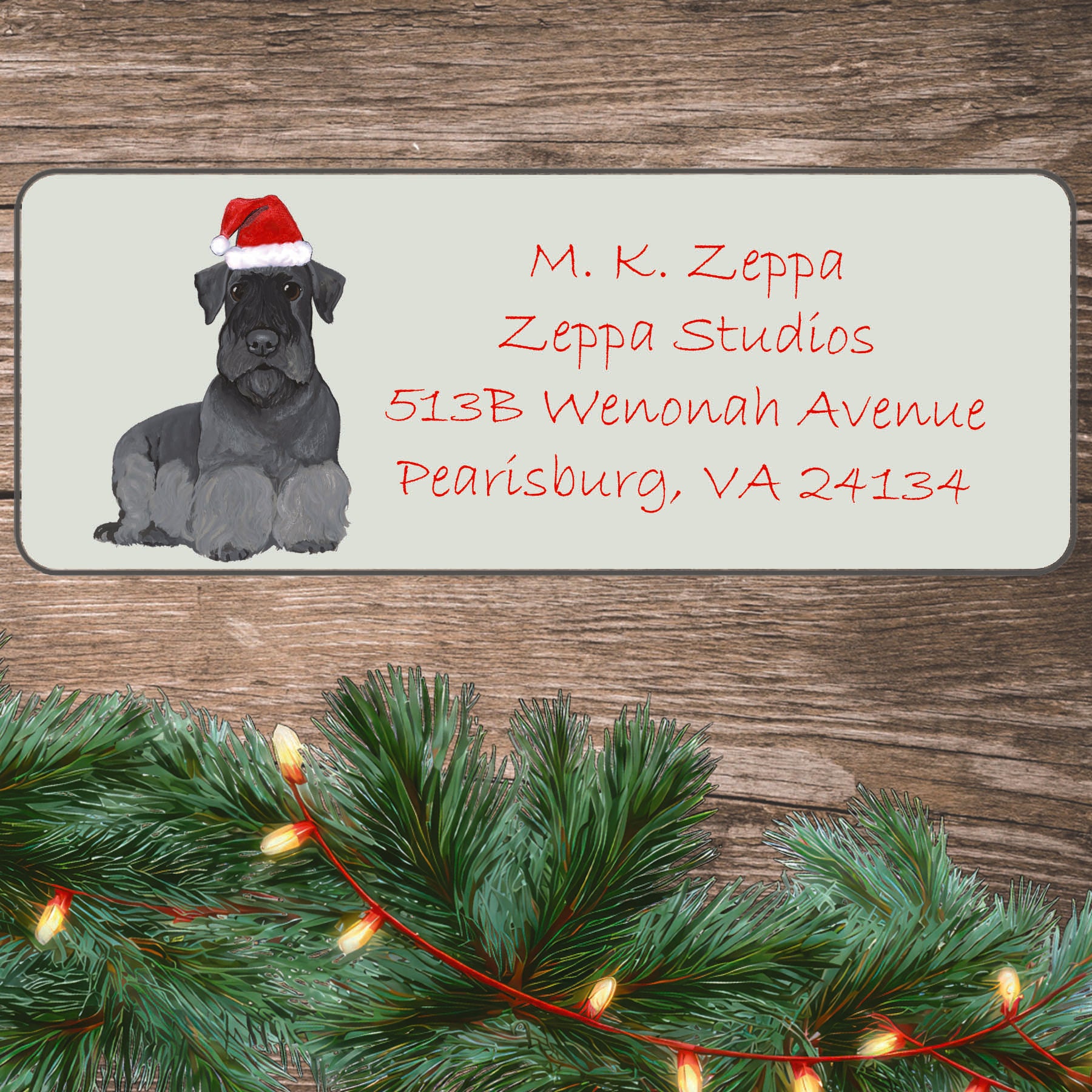 Cesky Terrier in a Santa Hat illustration on an ivory return address label set off by a wood surface with holiday greenery background.