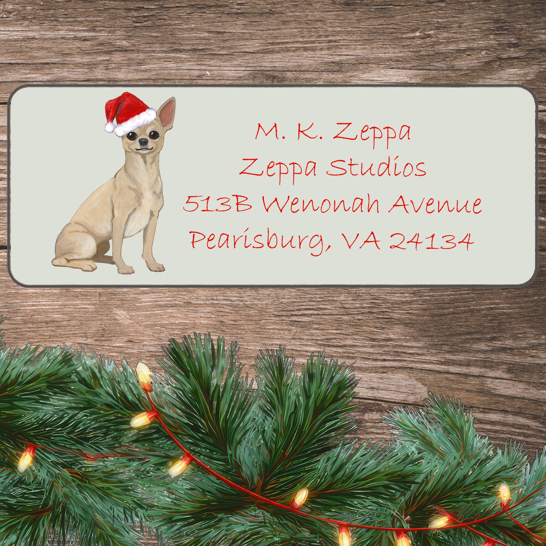 An illustration of a blonde Chihuahua wearing a Santa Hat on an ivory return address label set off by a wood surface with holiday greenery background.