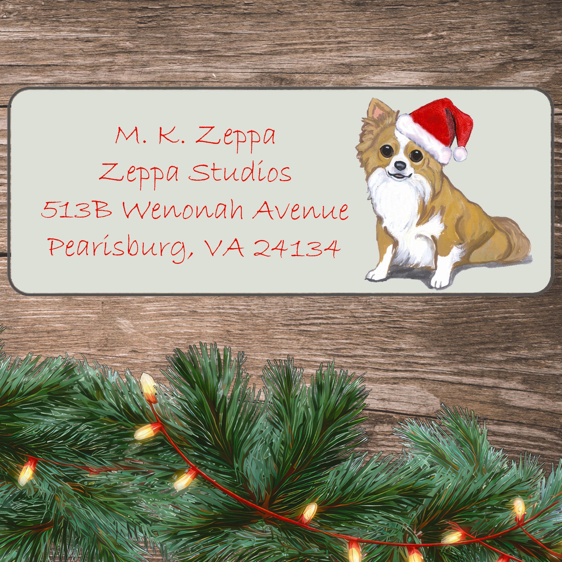 An illustration of a longhaired Chihuahua wearing a Santa Hat on an ivory return address label set off by a wood surface with holiday greenery background.