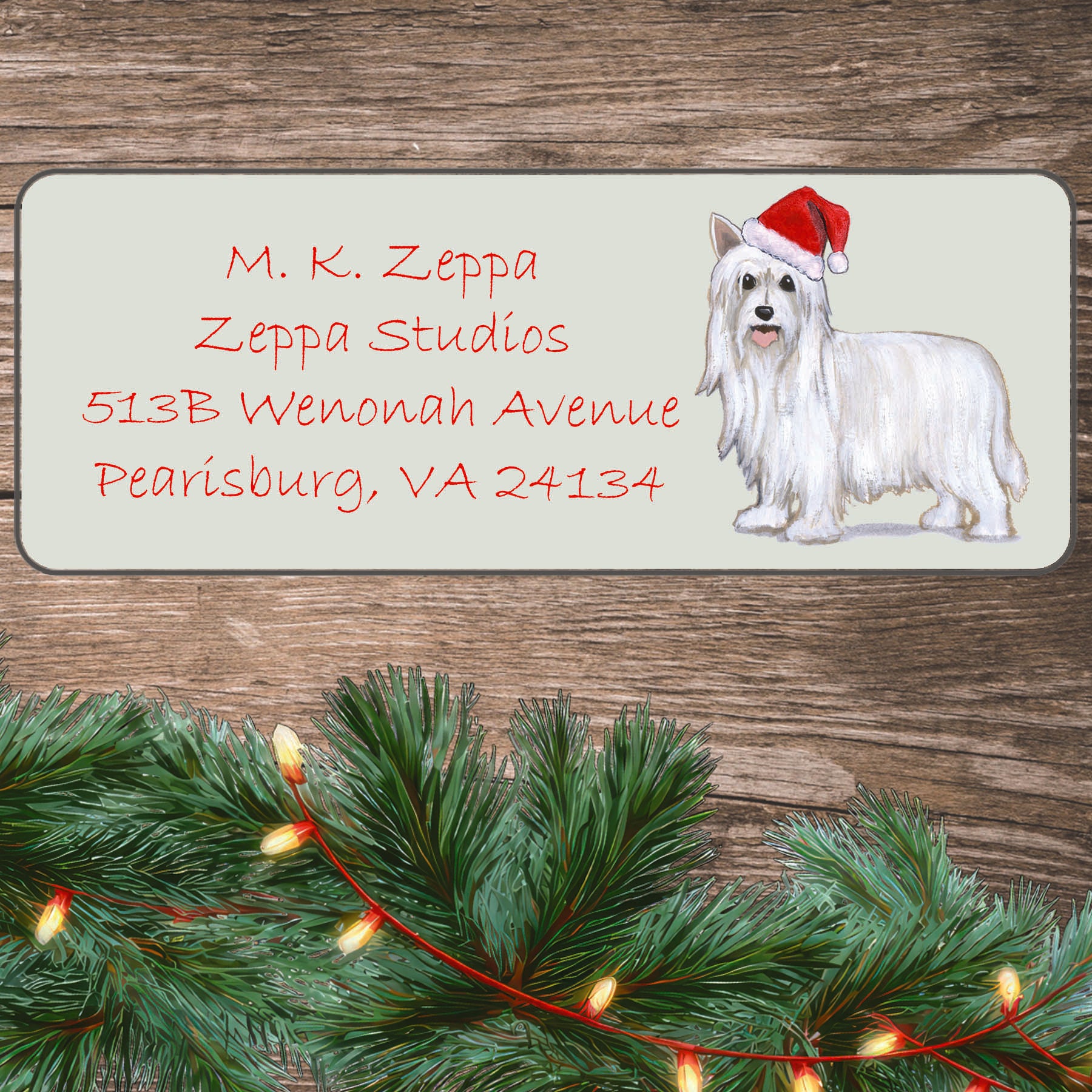 An illustration of a Powderpuff Chinese Crested wearing a Santa Hat on an ivory return address label set off by a wood surface with holiday greenery background.