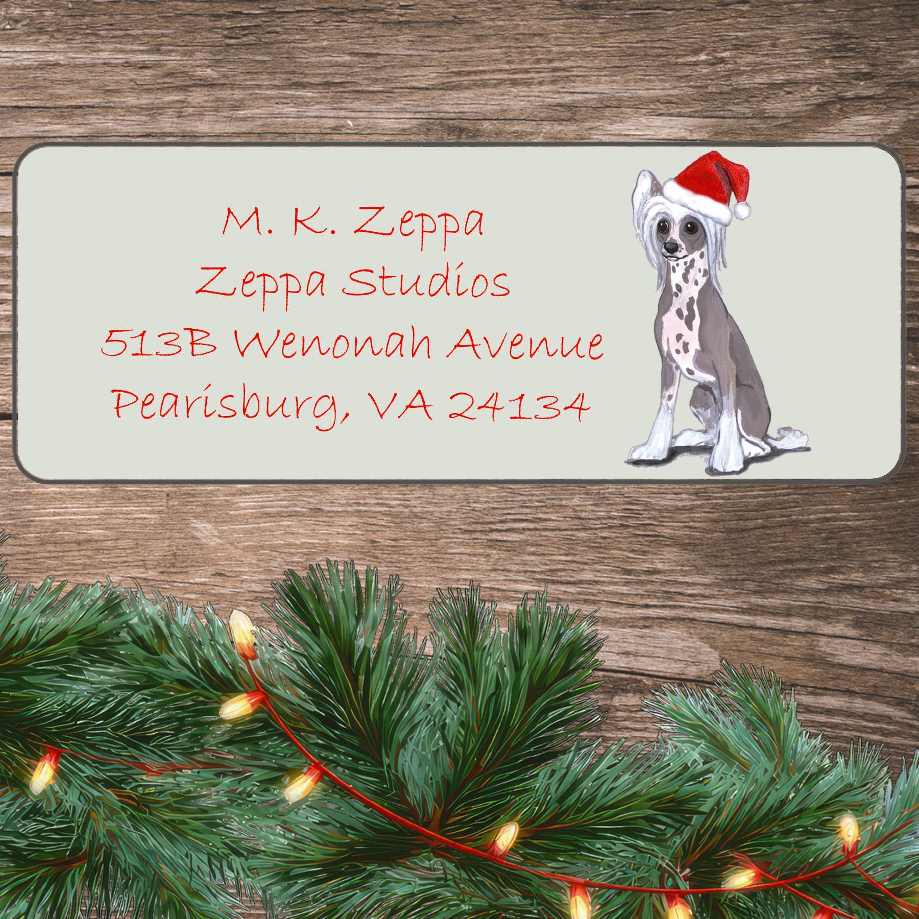An illustration of a Chinese Crested wearing a Santa Hat on an ivory return address label set off by a wood surface with holiday greenery background.