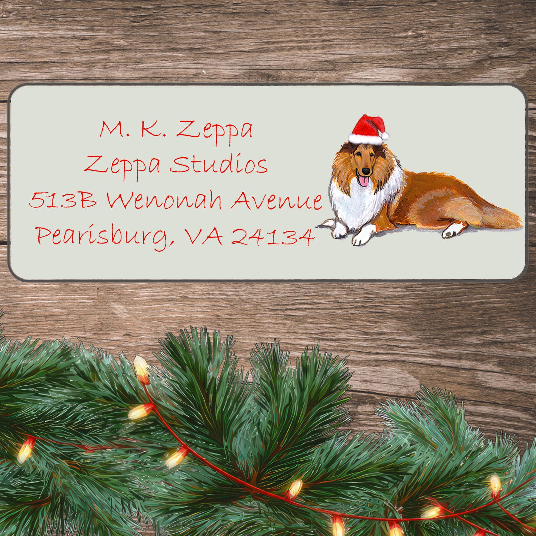 An illustration of a Collie wearing a Santa Hat on an ivory return address label set off by a wood surface with holiday greenery background.