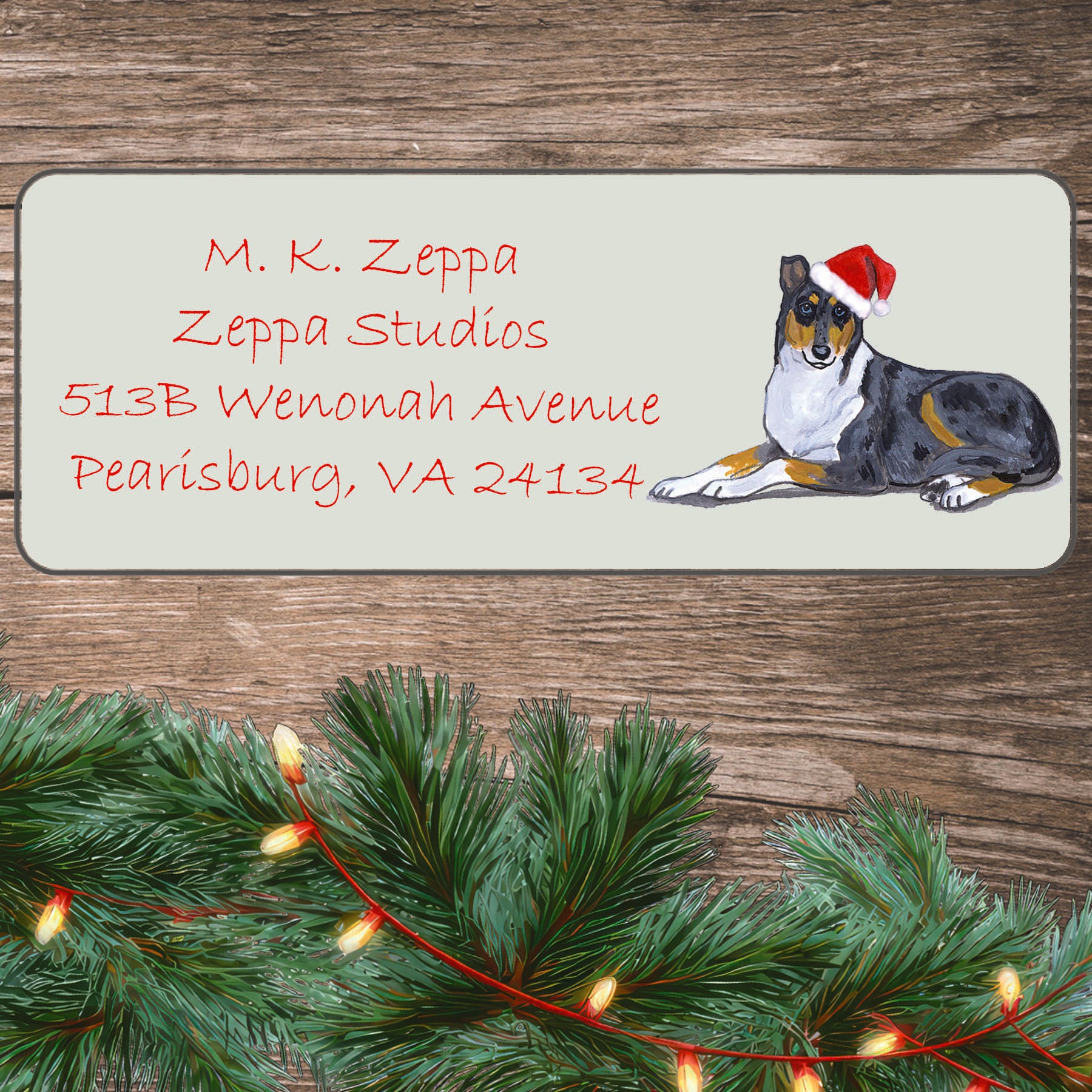 An illustration of a Smooth Collie wearing a Santa Hat on an ivory return address label set off by a wood surface with holiday greenery background.