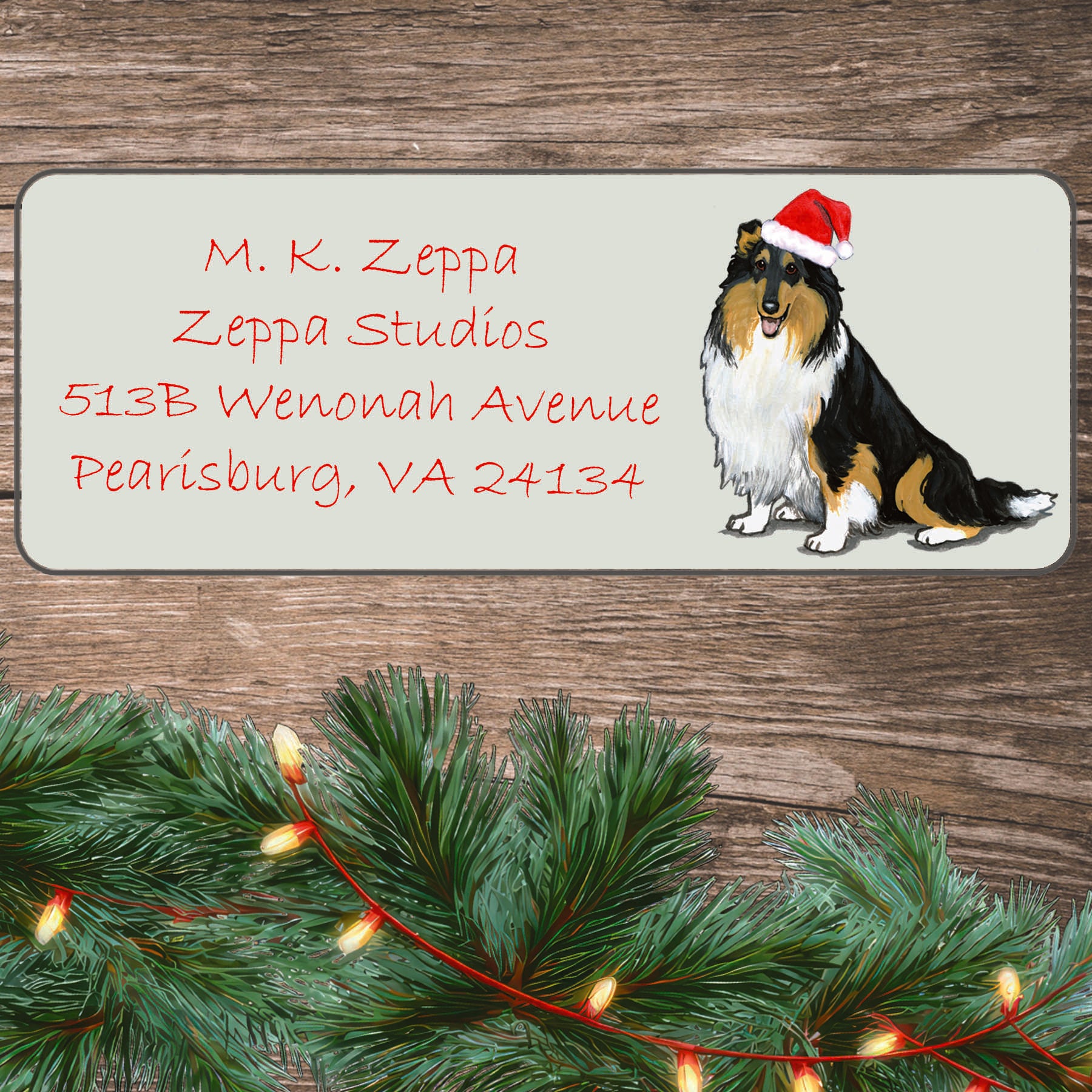 An illustration of a tri color rough Collie wearing a Santa Hat on an ivory return address label set off by a wood surface with holiday greenery background.