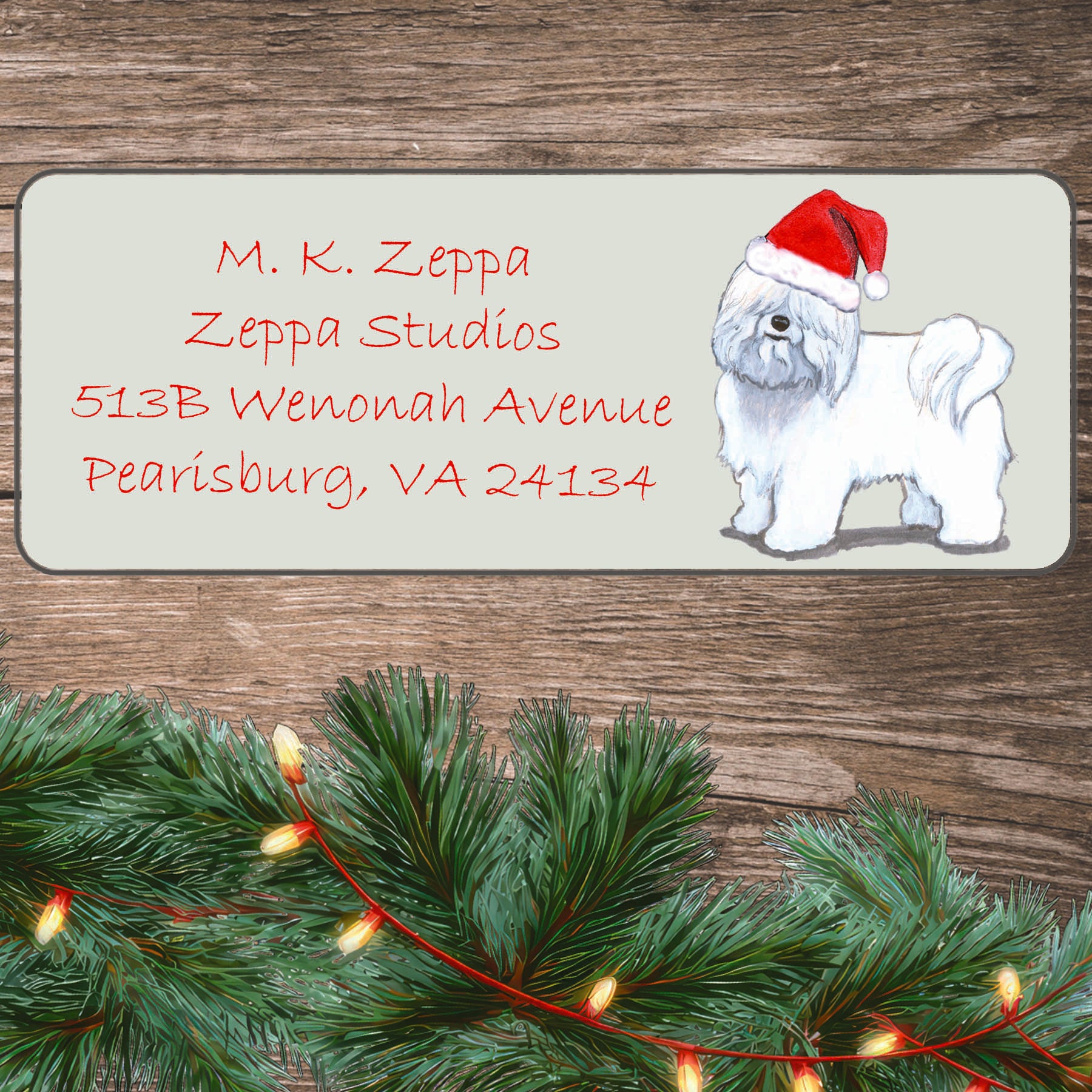 An illustration of a Coton du Tulear wearing a Santa Hat on an ivory return address label set off by a wood surface with holiday greenery background.