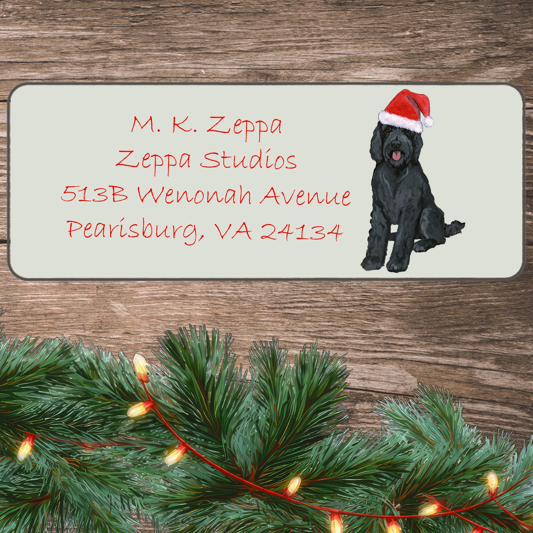 An illustration of a black Labradoodle wearing a Santa Hat on an ivory return address label set off by a wood surface with holiday greenery background.