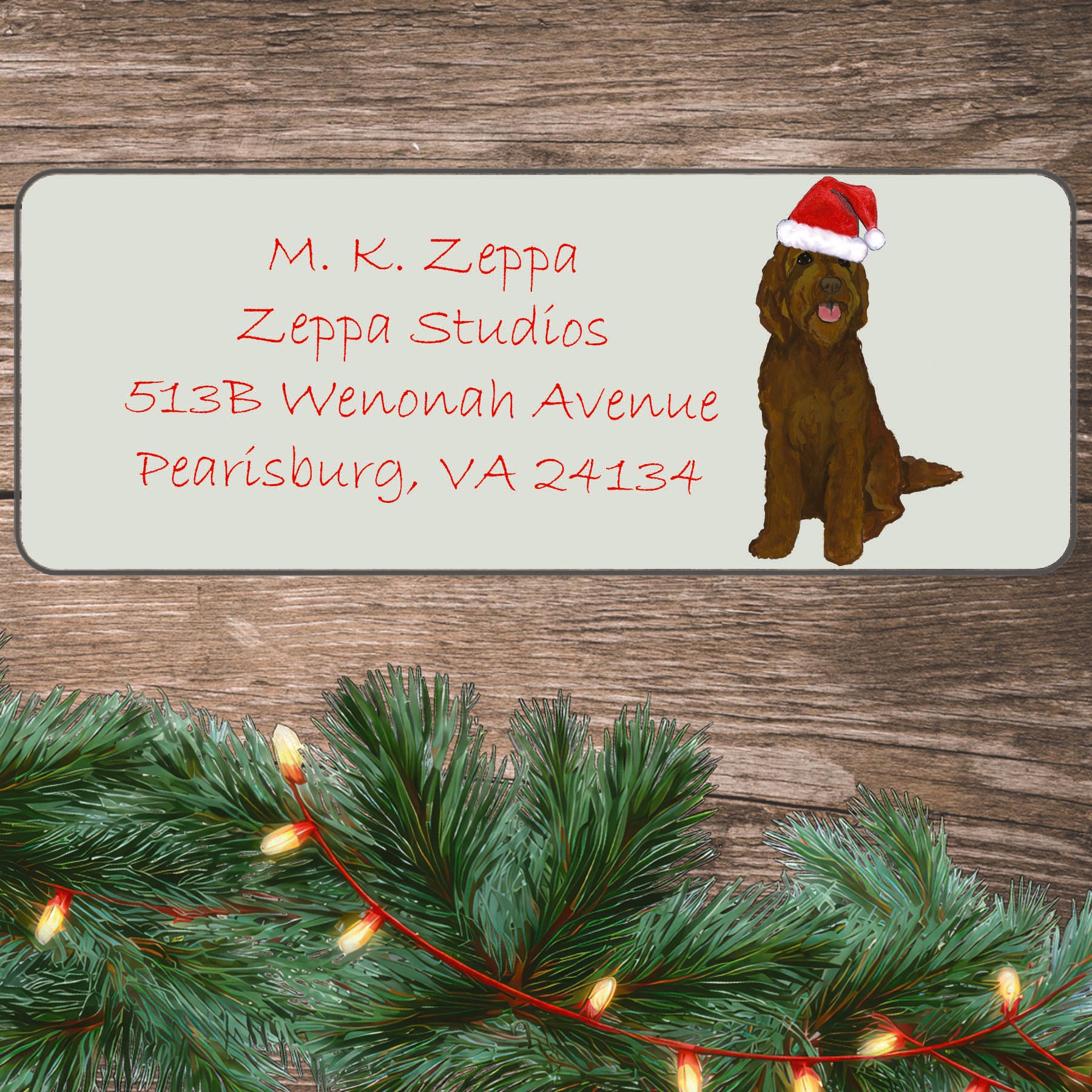An illustration of a brown Labradoodle  wearing a Santa Hat on an ivory return address label set off by a wood surface with holiday greenery background.