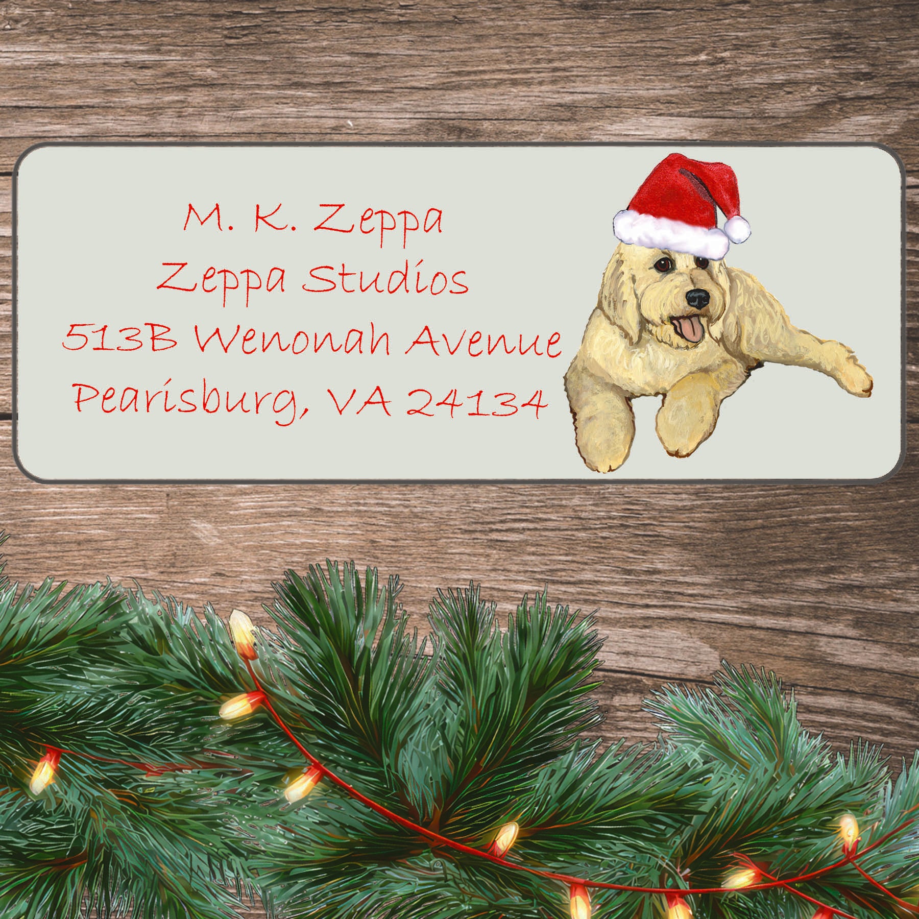 An illustration of a Golden Doodle wearing a Santa Hat on an ivory return address label set off by a wood surface with holiday greenery background.