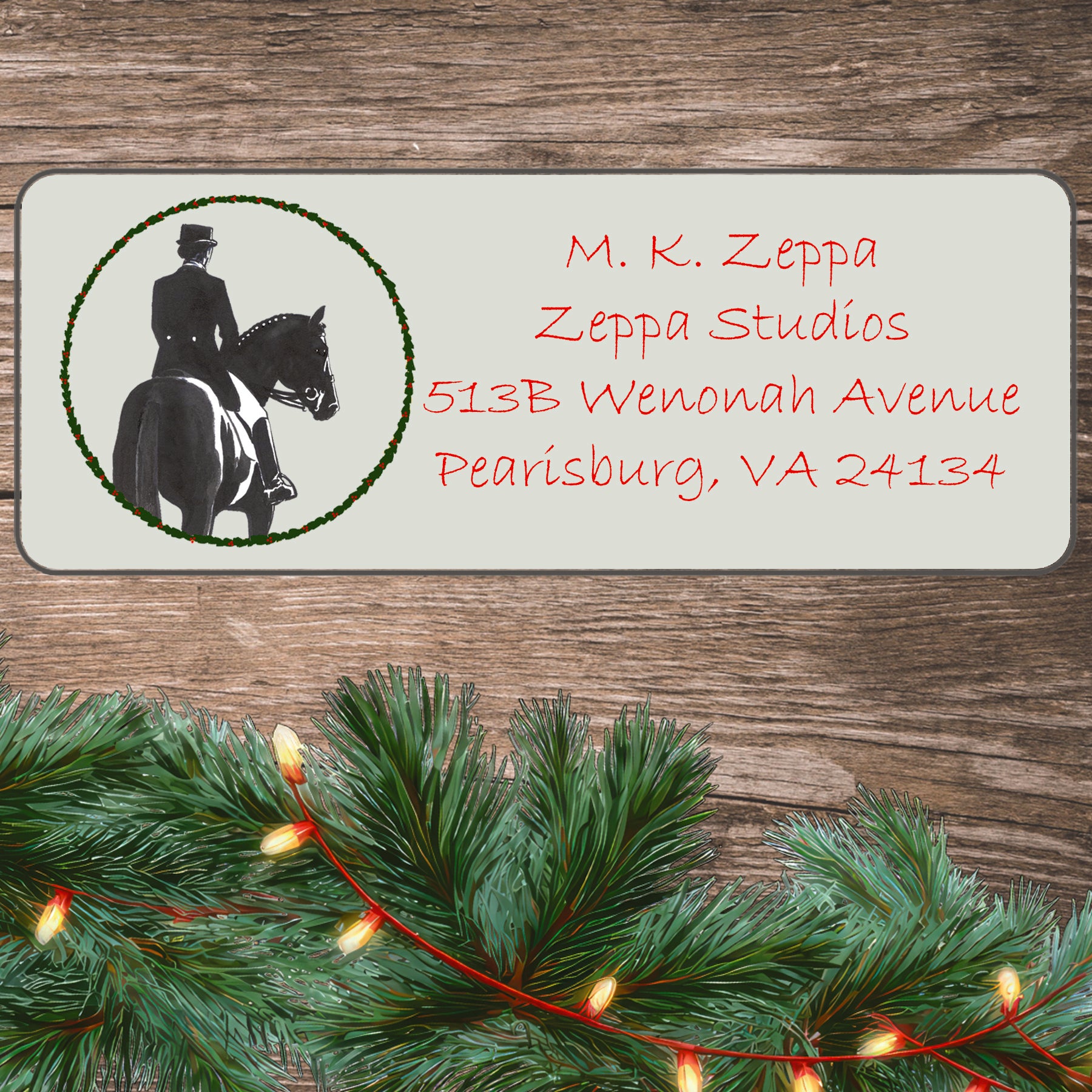 An illustration of a Dressage Horse and RIder surrounded by a holly wreath on an ivory return address label set off by a wood surface with holiday greenery background.