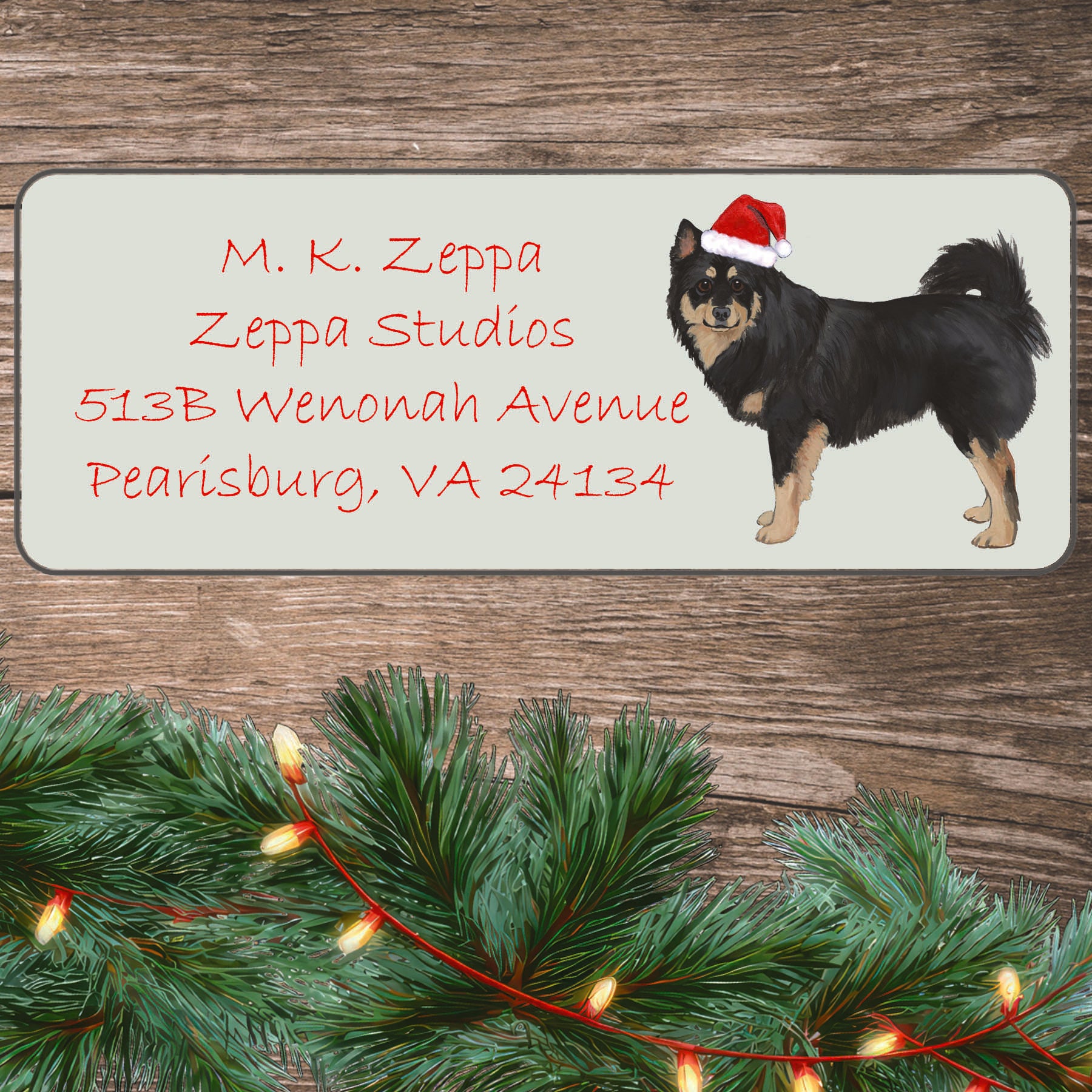 An illustration of a Finnish Lapphund wearing a Santa Hat on an ivory return address label set off by a wood surface with holiday greenery background.