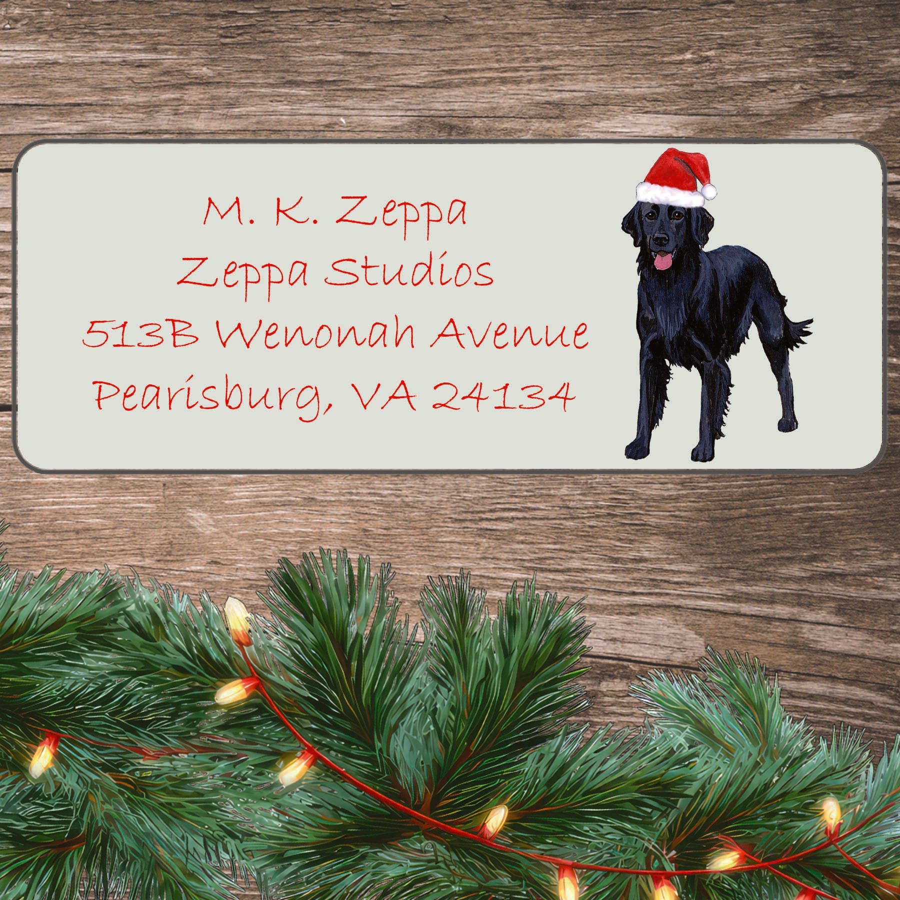 An illustration of a Flat Coated Retriever wearing a Santa Hat on an ivory return address label set off by a wood surface with holiday greenery background.